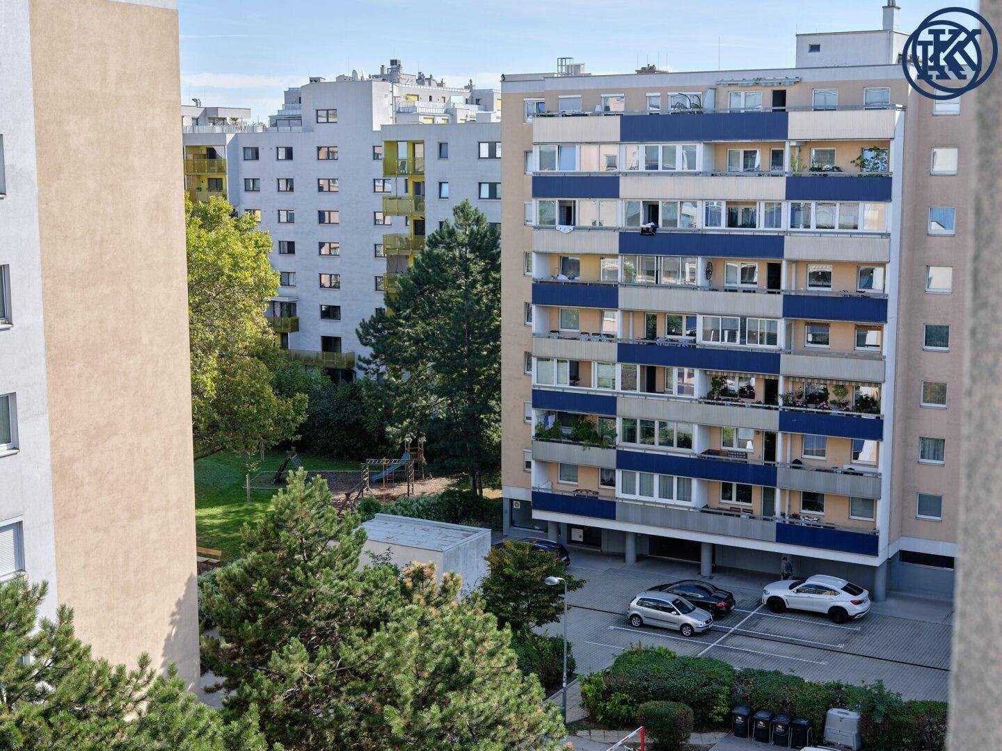 Blick auf Wohngebäude mit bunten Fassaden, einen Spielplatz, Bäume und geparkte Autos.