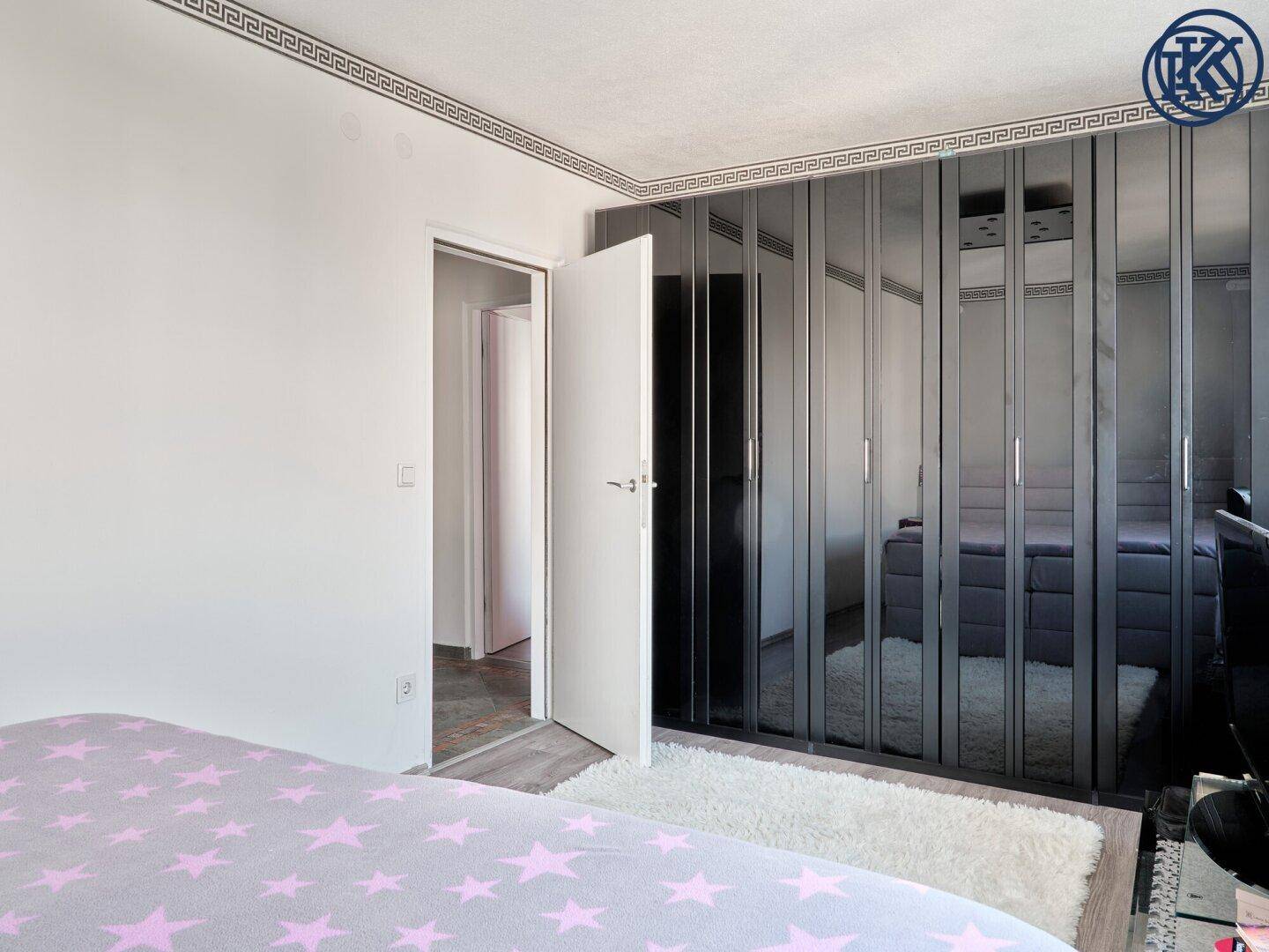 Schlafzimmer mit Bett und großem, modernen Spiegelschrank.
