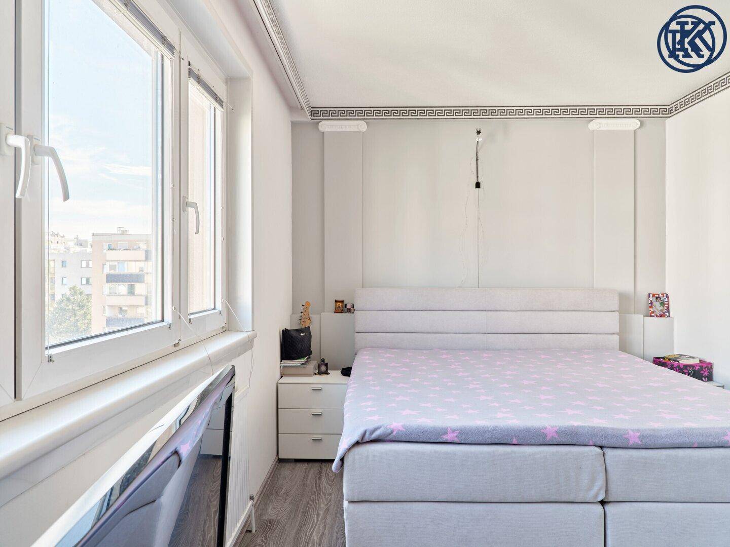 Schlafzimmer mit Bett und großen Fenstern, die viel Tageslicht hereinlassen.