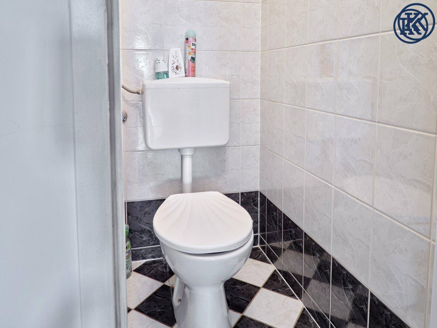 Separates WC mit Toilette und schwarz-weiß gefliestem Boden.