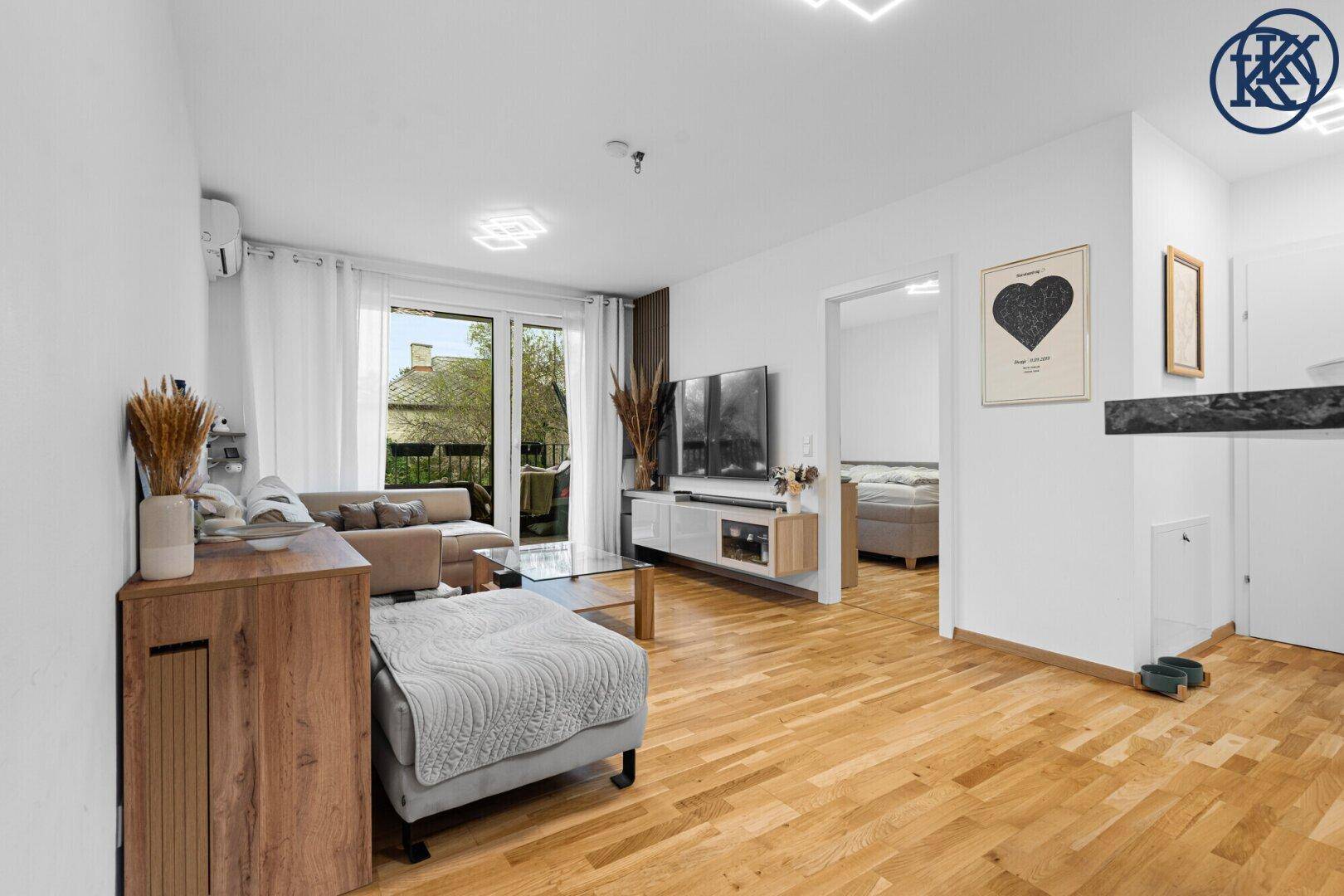 Gemütliches Wohnzimmer mit Holzboden, Balkonzugang und Blick in ein angrenzendes Schlafzimmer.