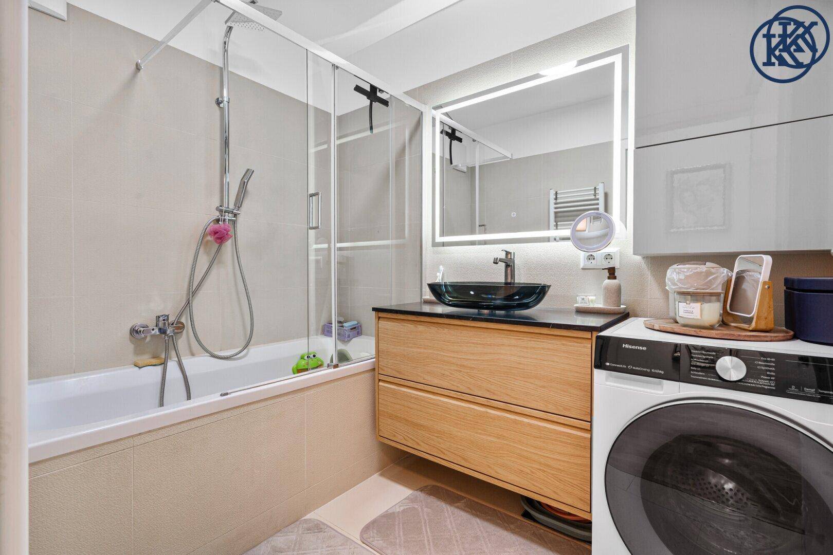 Modernes Badezimmer mit Badewanne, Duschwand, stilvollem Waschtisch und Waschmaschine.