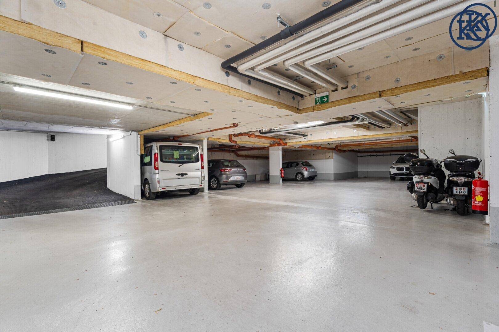 Helle Tiefgarage mit mehreren Stellplätzen für Autos und Motorroller.