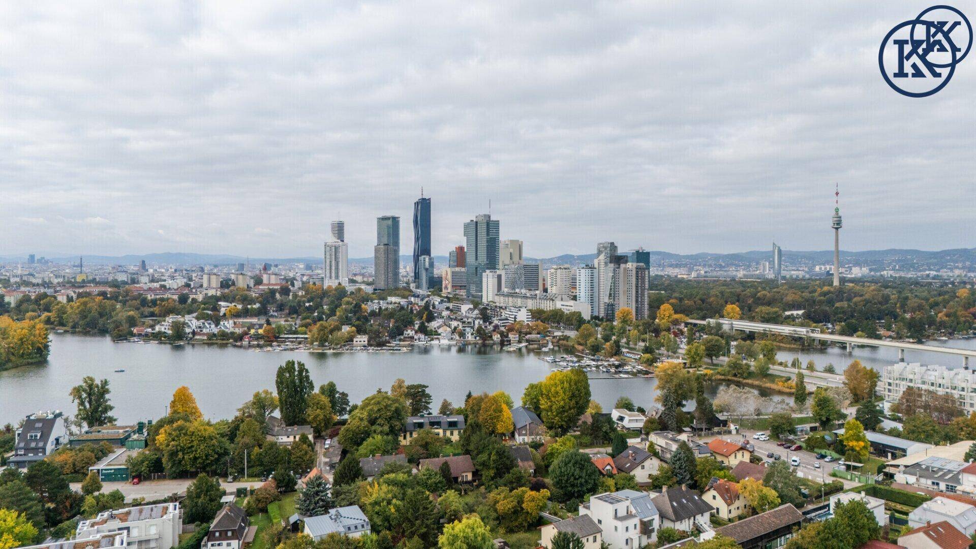 Panoramablick auf die Stadt mit See, Hochhäusern und Wohngebieten unter bewölktem Himmel.