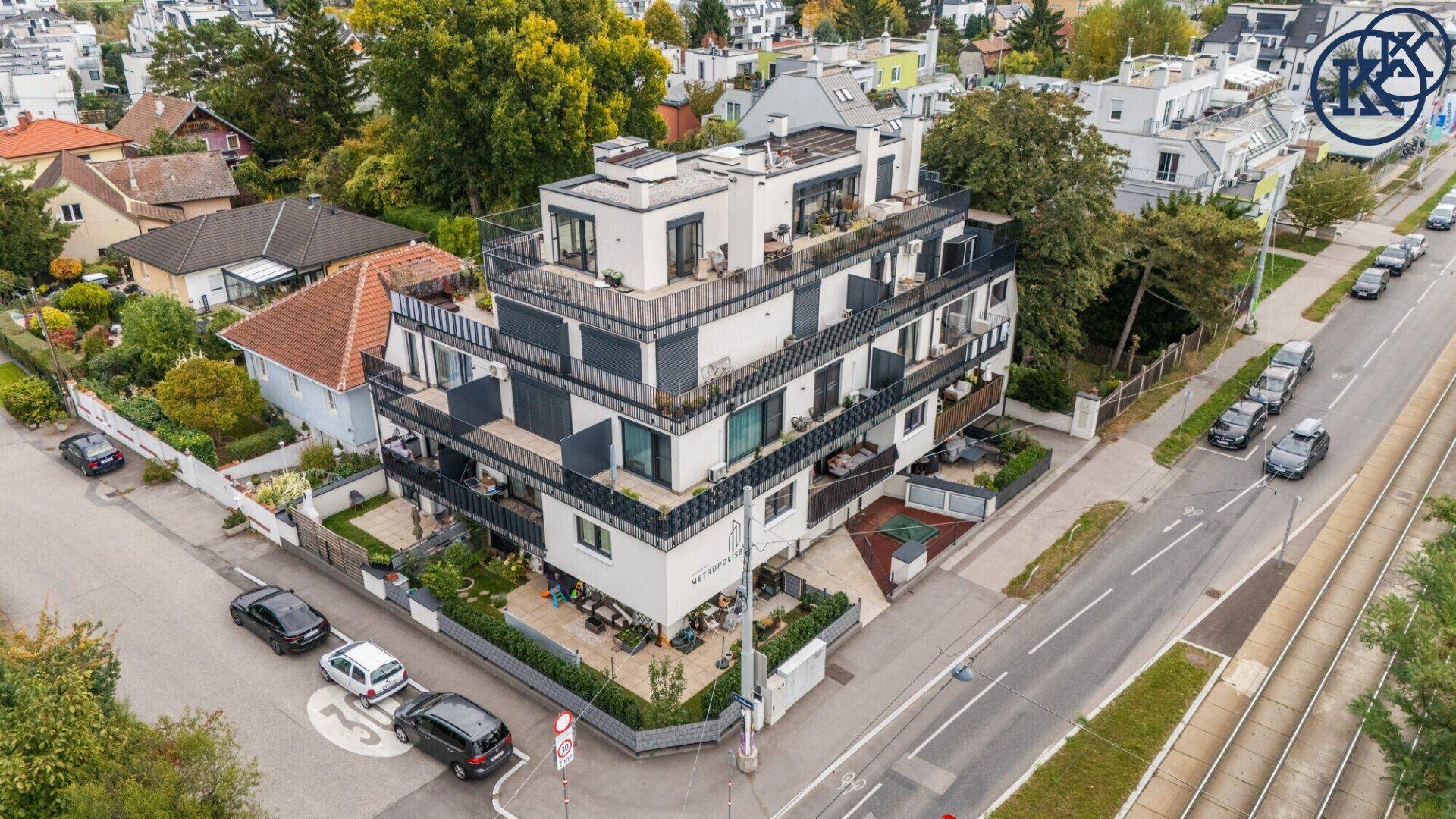 Luftaufnahme eines Eckgebäudes mit moderner Architektur, Balkonen und umliegender Straße.