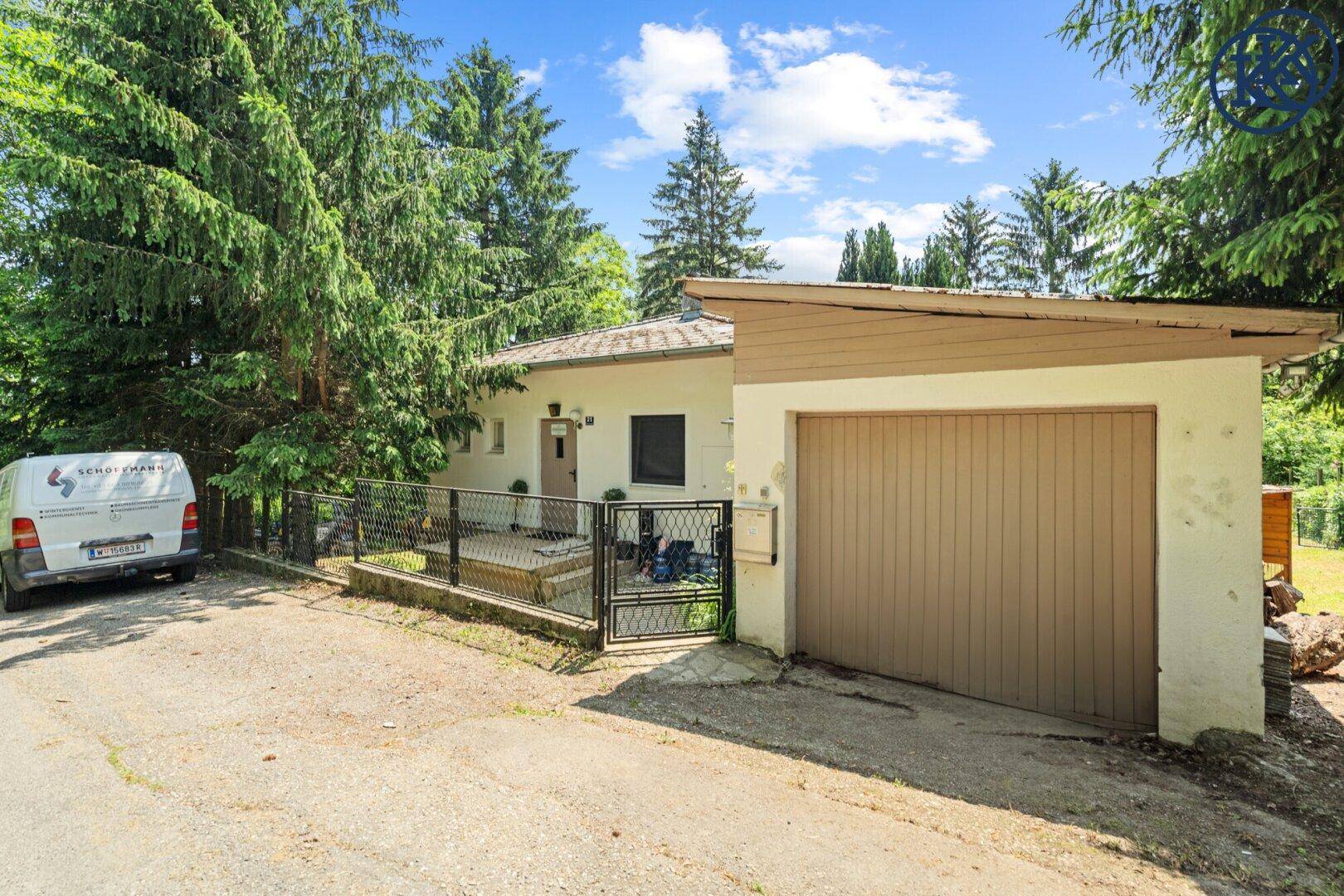 Einfahrt zum Haus mit Garage und einem gepflegten Vorgartenbereich, umgeben von viel Grün.