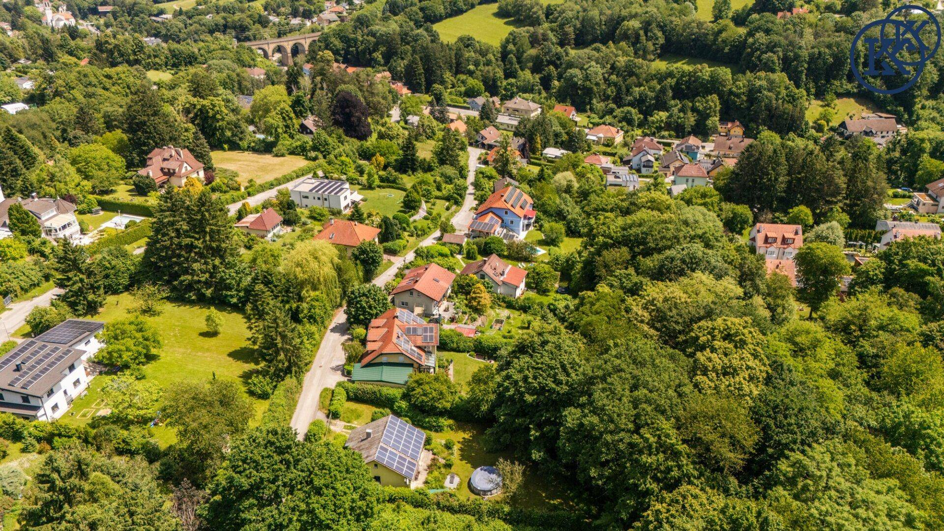 Weitläufige Luftaufnahme einer grünen Wohnsiedlung mit vielen Häusern und Bäumen unter blauem Himmel.