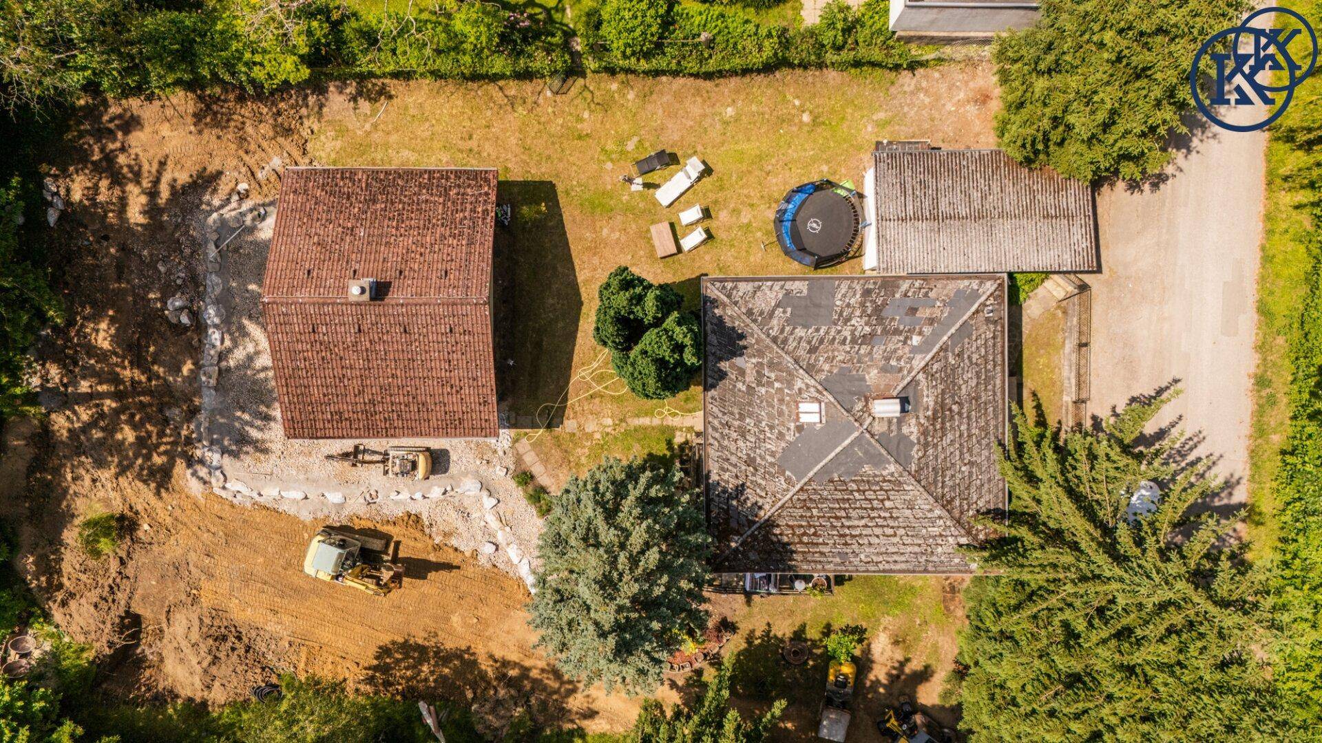 Überblick über zwei Häuser mit großem Garten, Trampolin und Baustellenaktivitäten aus der Vogelperspektive.