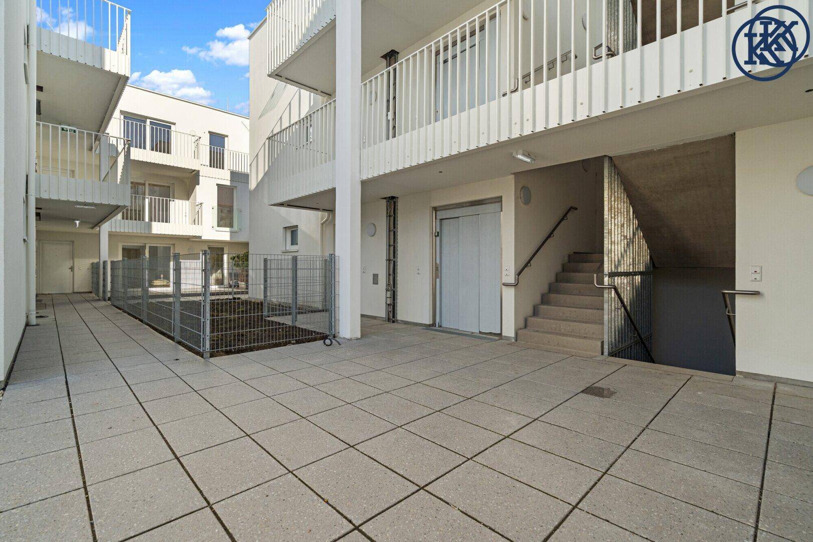 Außenbereich eines modernen Gebäudes mit Fliesenboden, Aufzug und Treppenhauszugang.