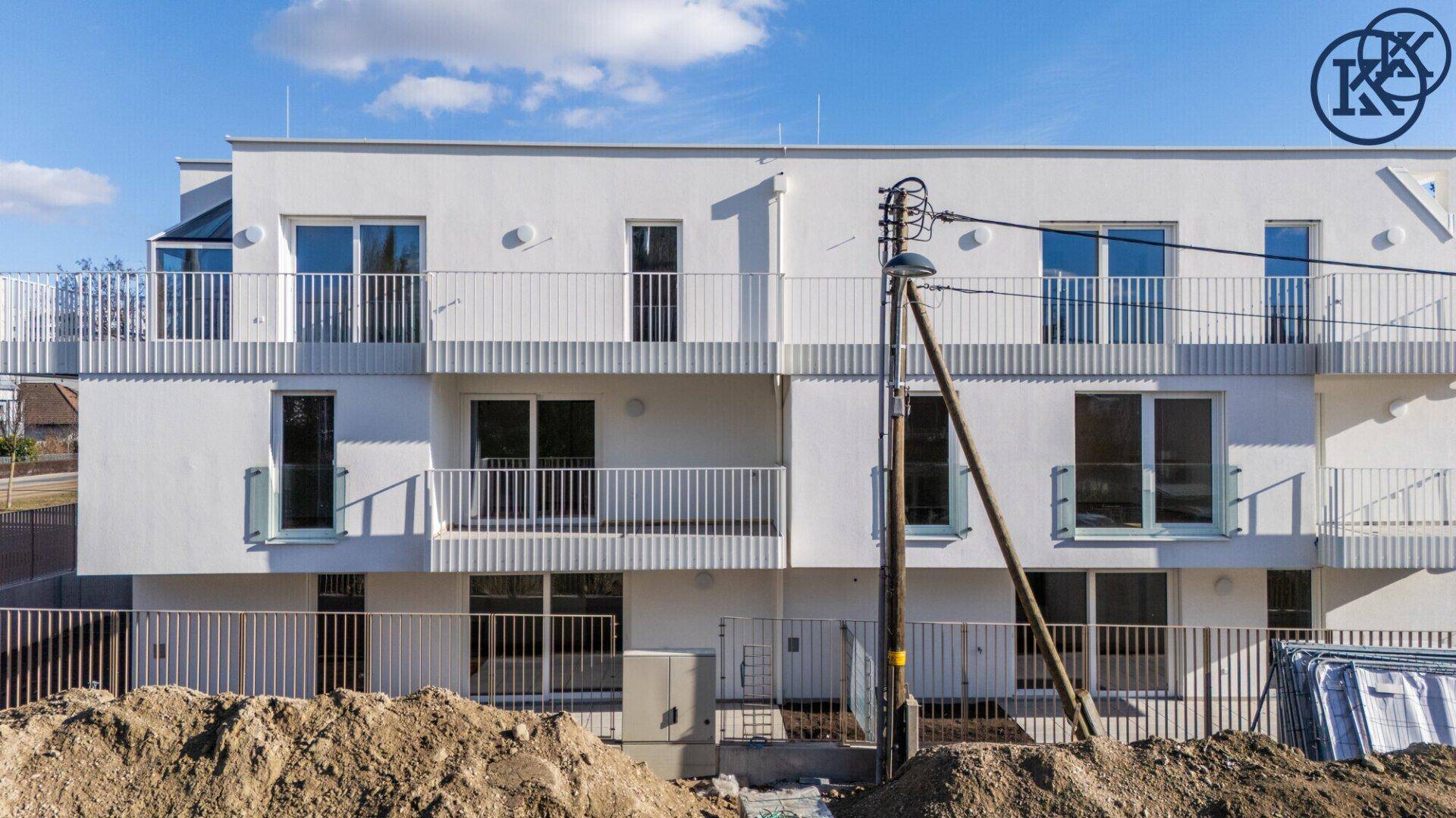 Vorderansicht des modernen Wohngebäudes mit Balkonen und Baustellenbereich im Vordergrund.