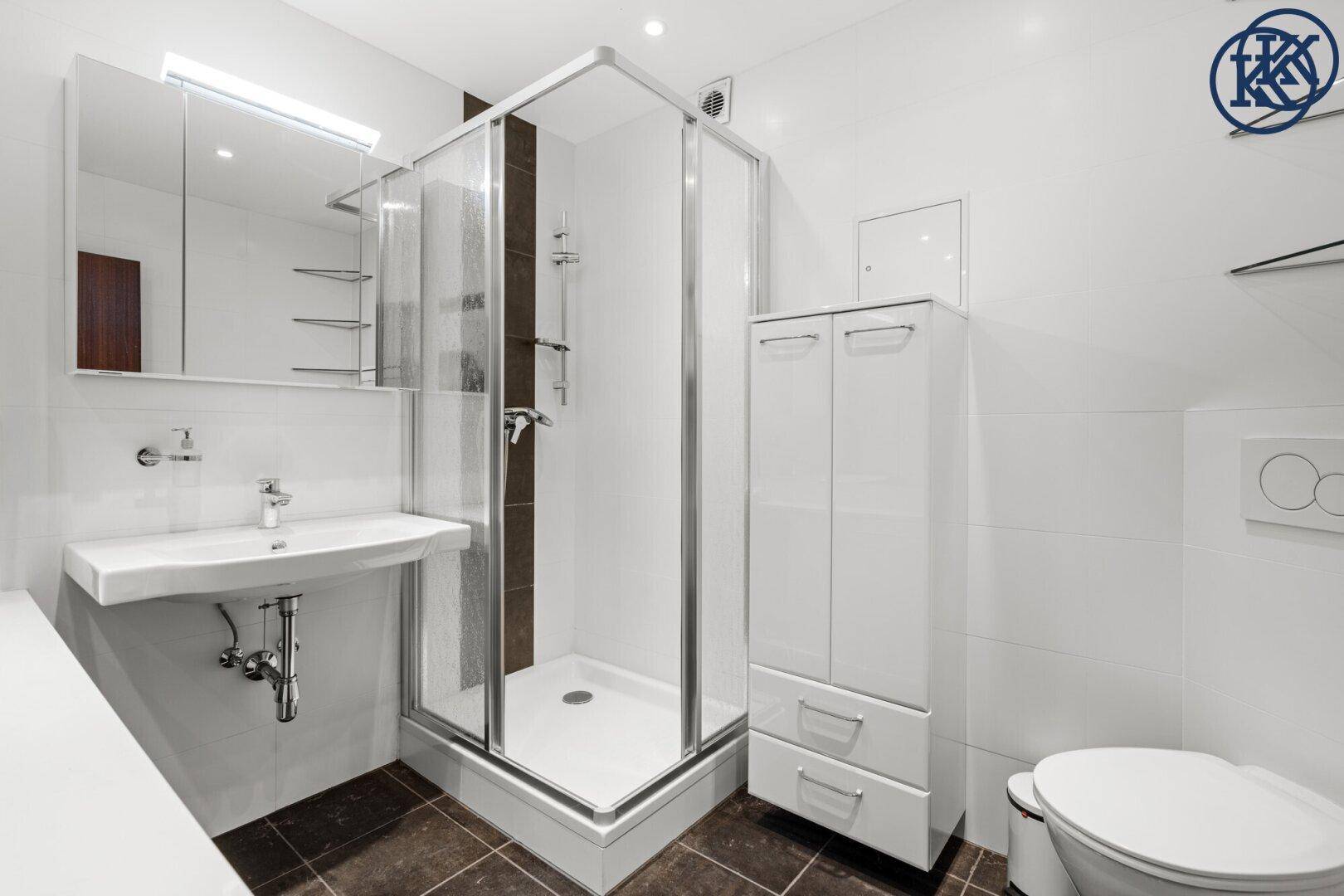 Modernes Badezimmer mit Duschkabine, Waschbecken und Toilette, weiße Fliesen und dunkler Boden.