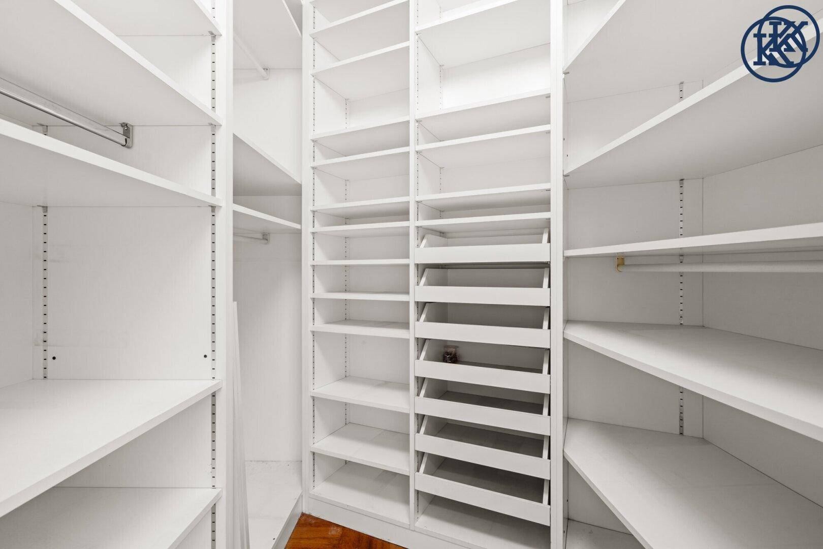 Begehbarer Kleiderschrank mit vielen weißen Regalen und Fächern für Kleidung und Accessoires.