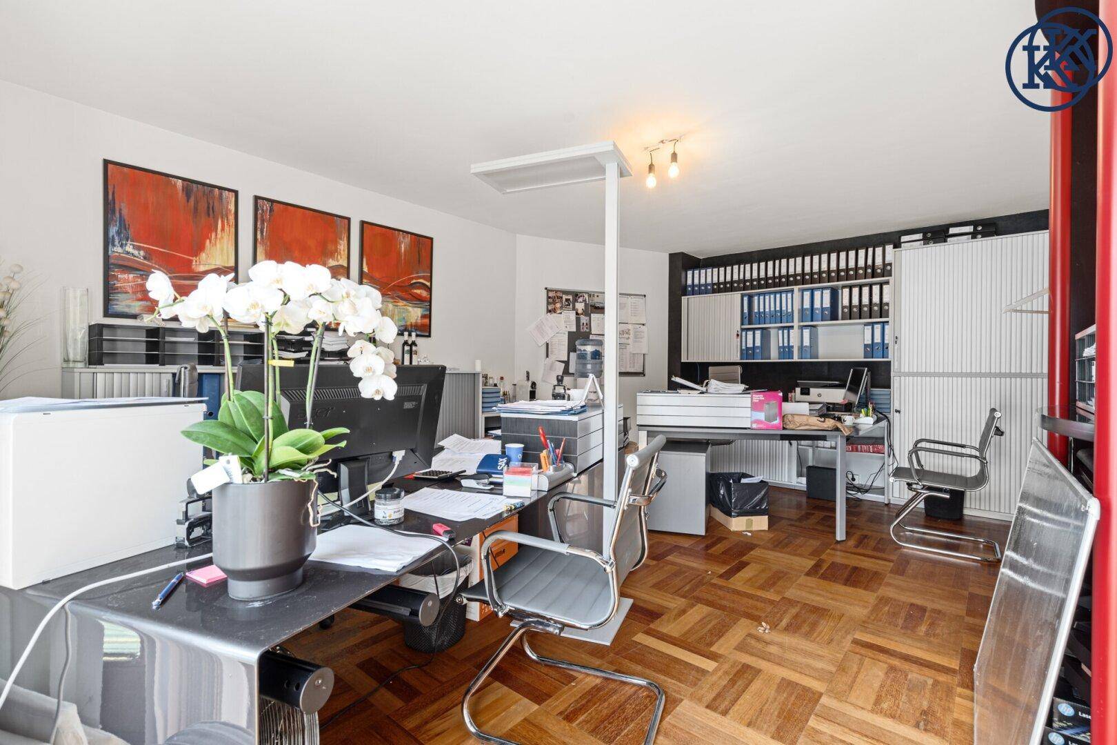 Eingerichtetes Büro mit Schreibtischen, Bürostühlen und Regalen, Kunstwerke an den Wänden.