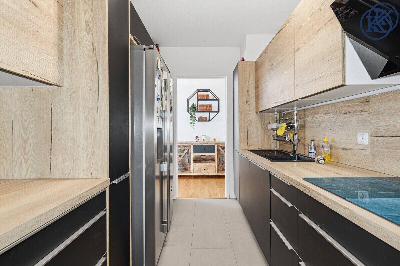 Lange, schmale Küche mit modernen Holz- und Schwarzfronten und Zugang zu einem weiteren Raum.