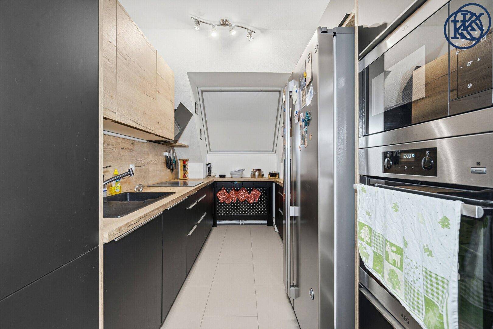 Moderne Küche mit schwarzen und holzfarbenen Schränken, Edelstahlgeräten und Dachfenster.