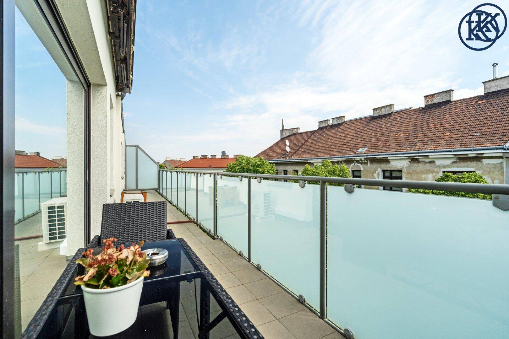 Möblierte Terrasse mit Sitzgelegenheiten und Pflanzen, Glasbrüstung und Blick auf die Umgebung.