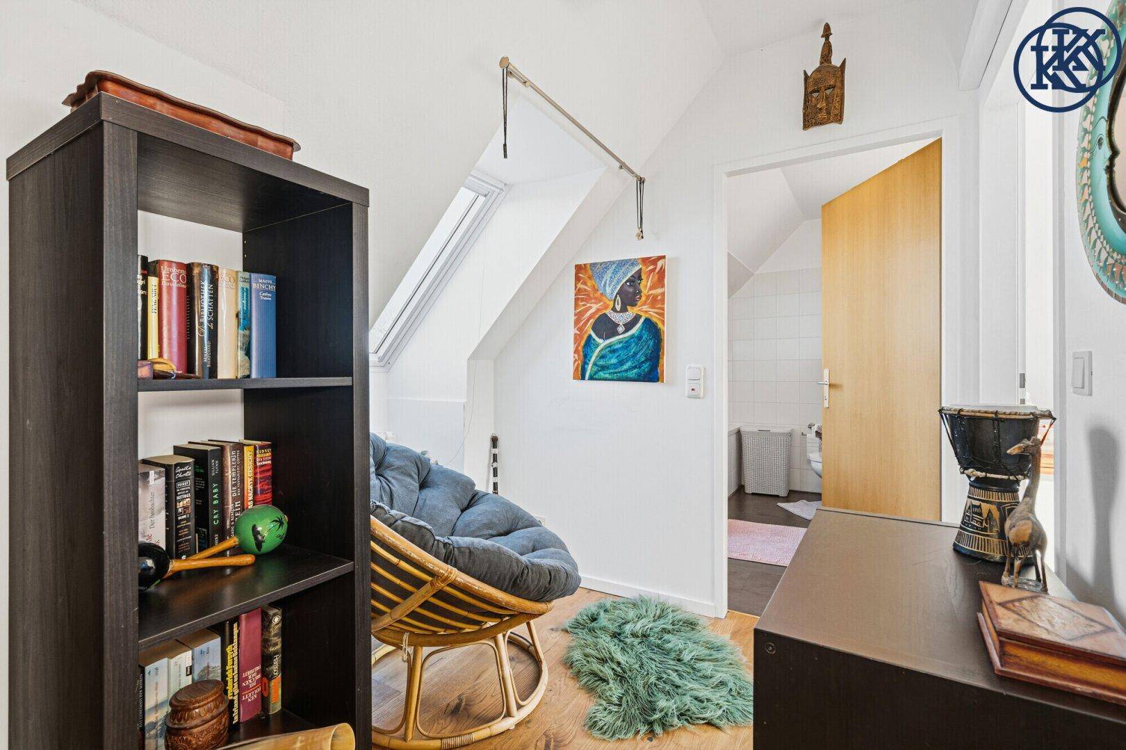 Gemütlicher Arbeitsbereich mit Dachschräge, Bücherregal und bequemen Sitzgelegenheiten.
