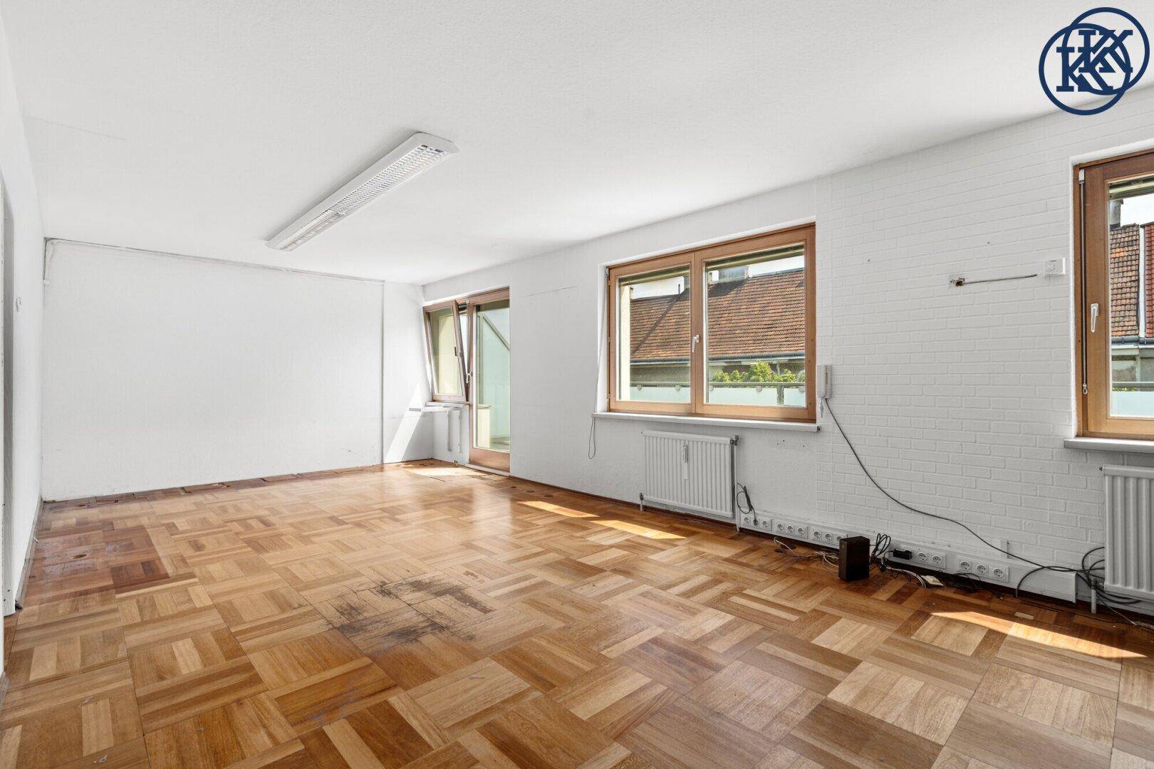 Geräumiger Büroraum mit Parkettboden und mehreren Fenstern, weiße Wände und viel Tageslicht.