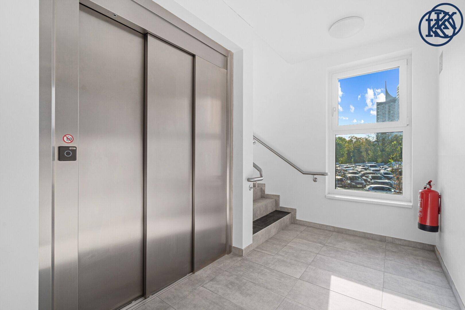 Moderner Aufzug in einem hellen Treppenhaus mit Fenster und Blick nach draußen.