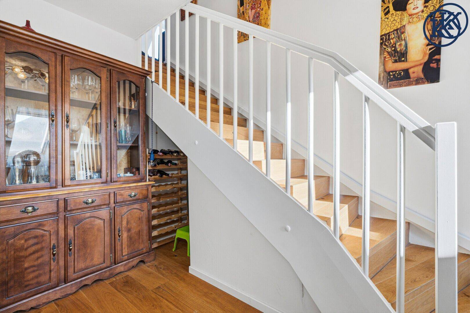 Holztreppe mit weißem Geländer und einem eleganten Holzschrank im Treppenhausbereich.