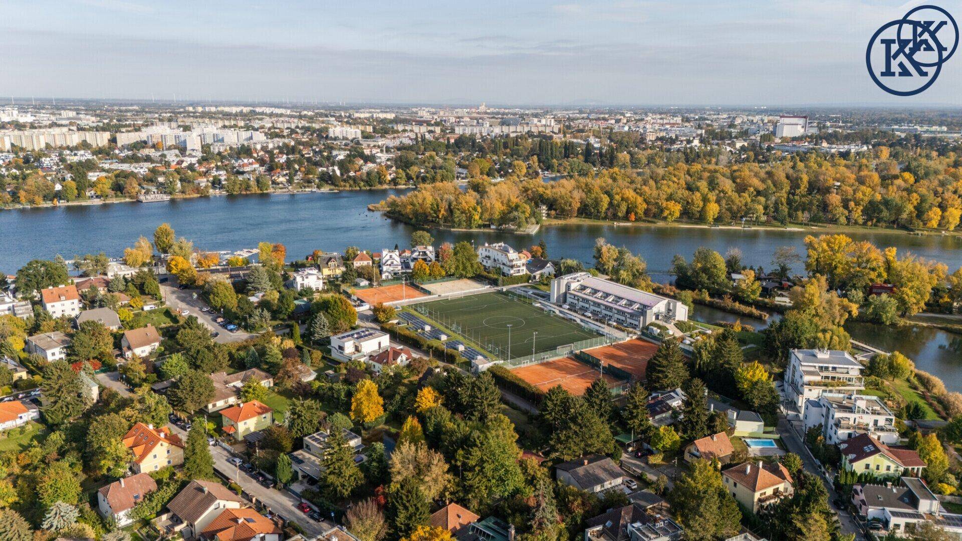Luftaufnahme einer Wohngegend mit See, viel Grün und Sportanlagen.