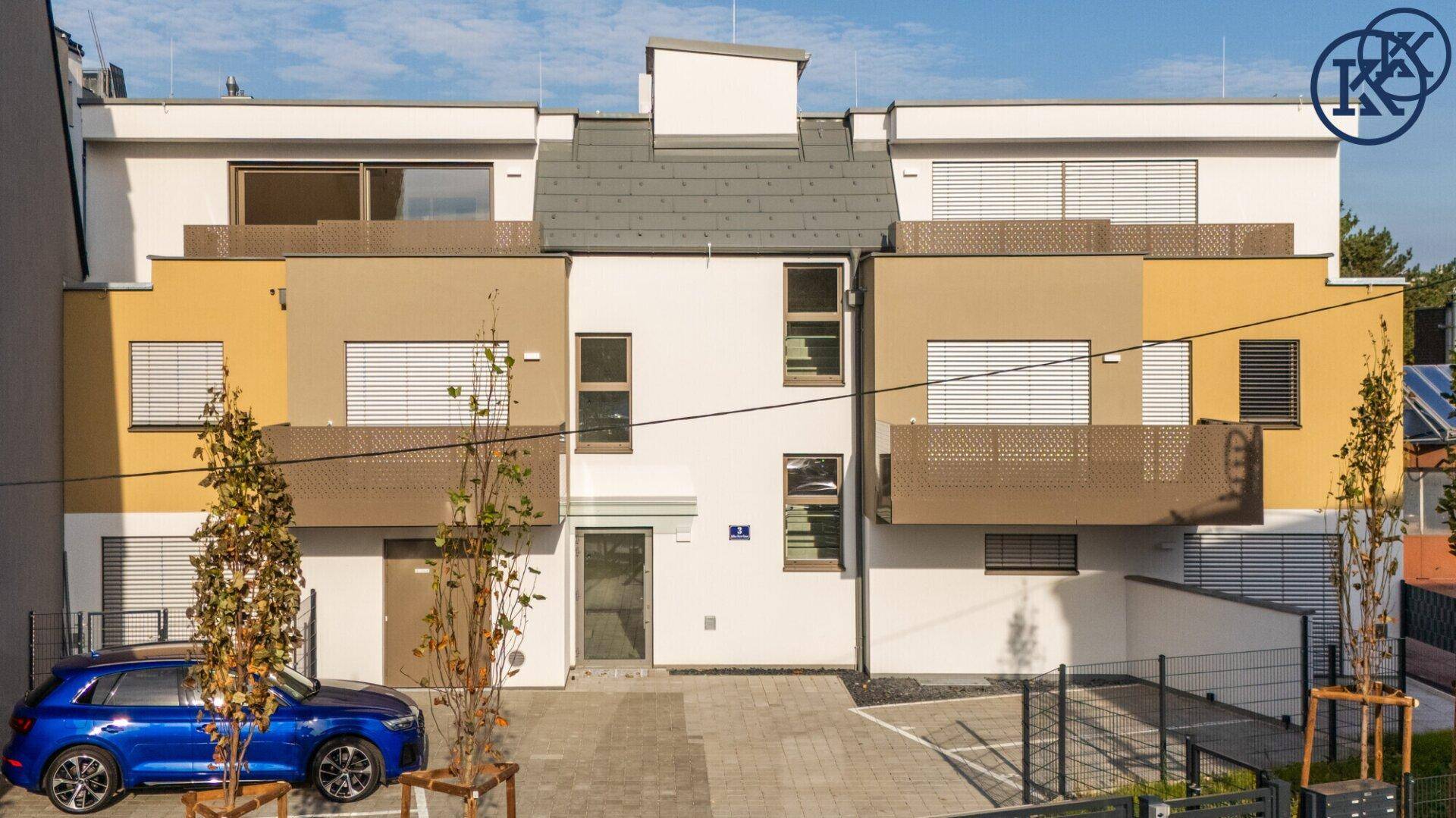 Moderne Wohnanlage mit mehrfarbiger Fassade, Balkonen und Außenparkplätzen vor blauem Himmel.