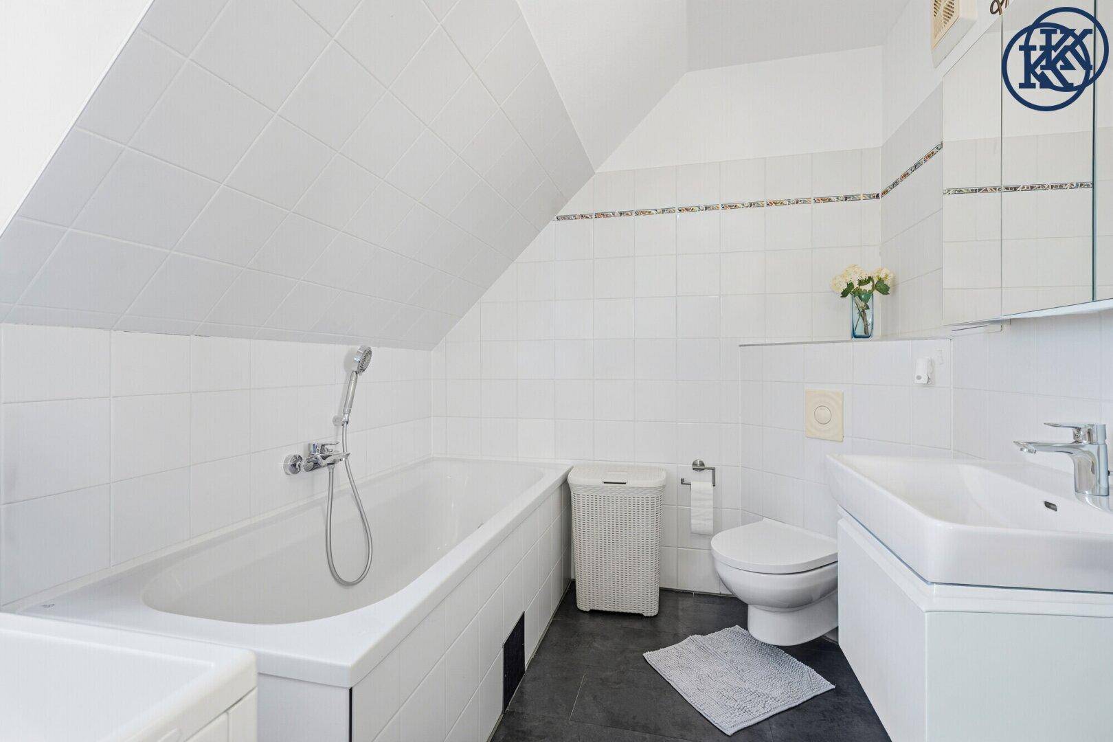 Helles Badezimmer mit Badewanne, WC, Waschbecken und weiß gefliesten Wänden unter der Dachschräge.