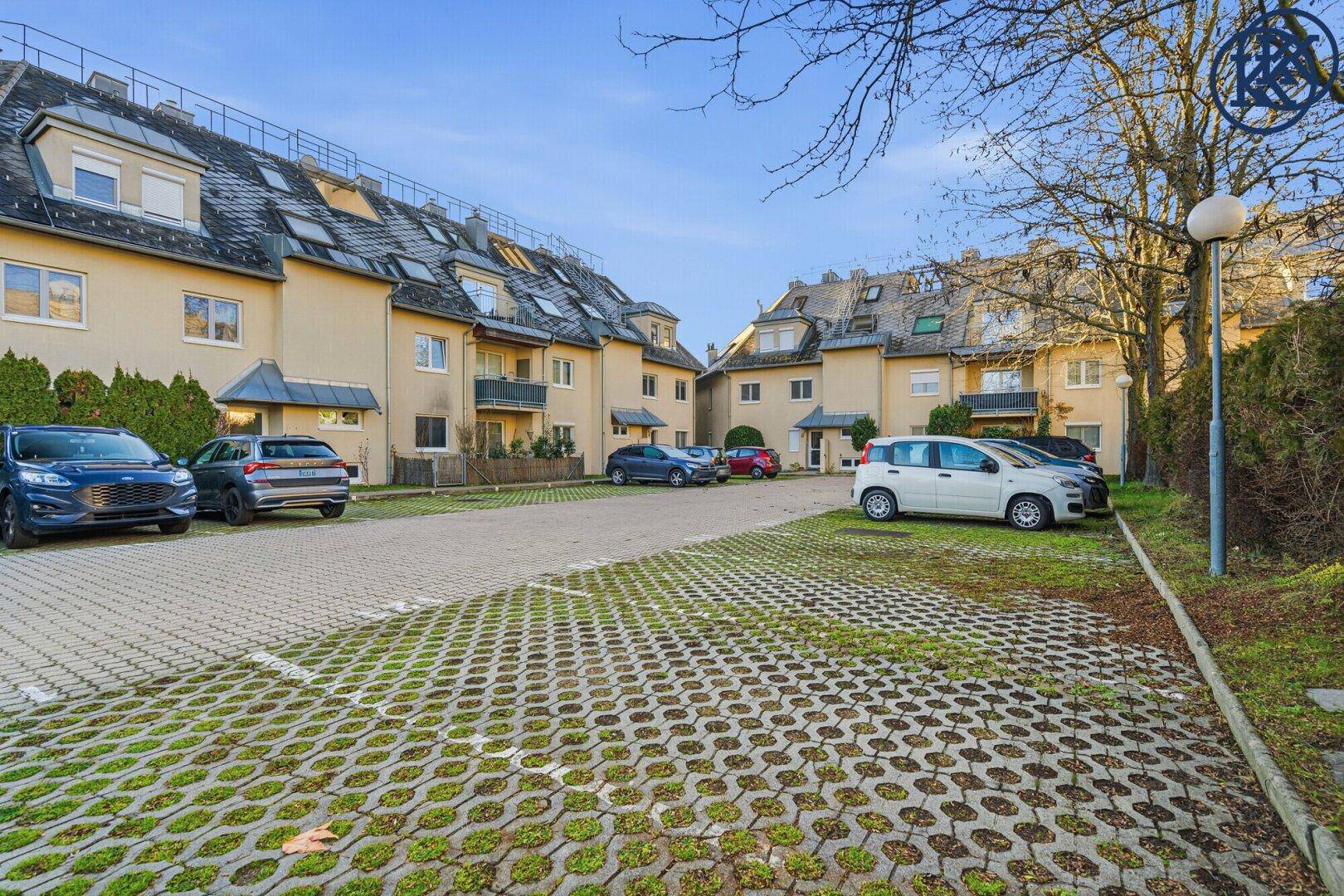 Wohnanlage mit mehreren Gebäuden und umweltfreundlichen Parkflächen mit Rasengittersteinen.
