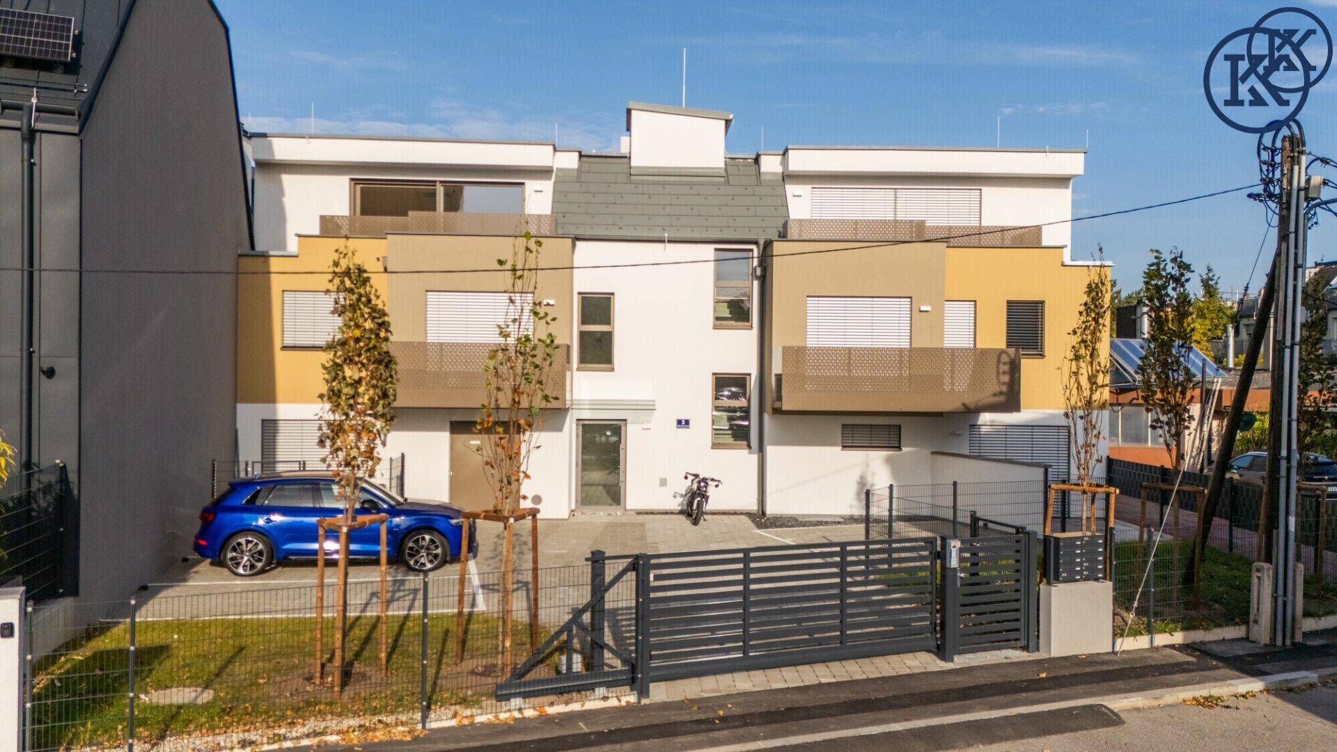Gesamtansicht der modernen Wohnanlage von der Straße aus mit Zaun und jungen Bäumen.