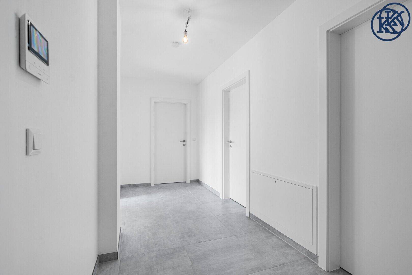 Moderner Flur mit grauen Fliesen, weißen Wänden und einer Gegensprechanlage an der Wand.