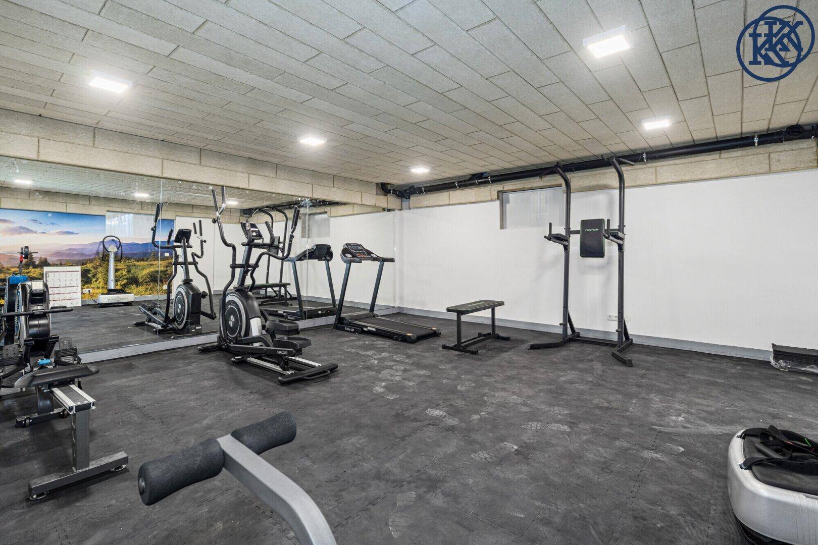 Gut ausgestatteter Fitnessraum mit verschiedenen Trainingsgeräten und Spiegelflächen.