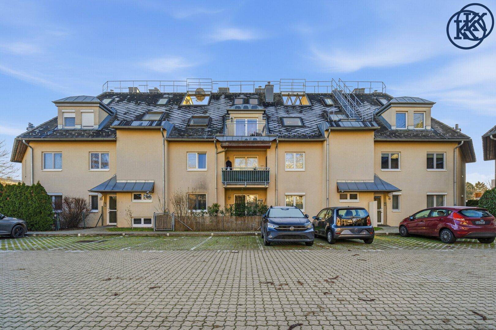 Mehrfamilienhaus mit mehreren Wohneinheiten und Parkplätzen vor der Fassade an einem klaren Tag.