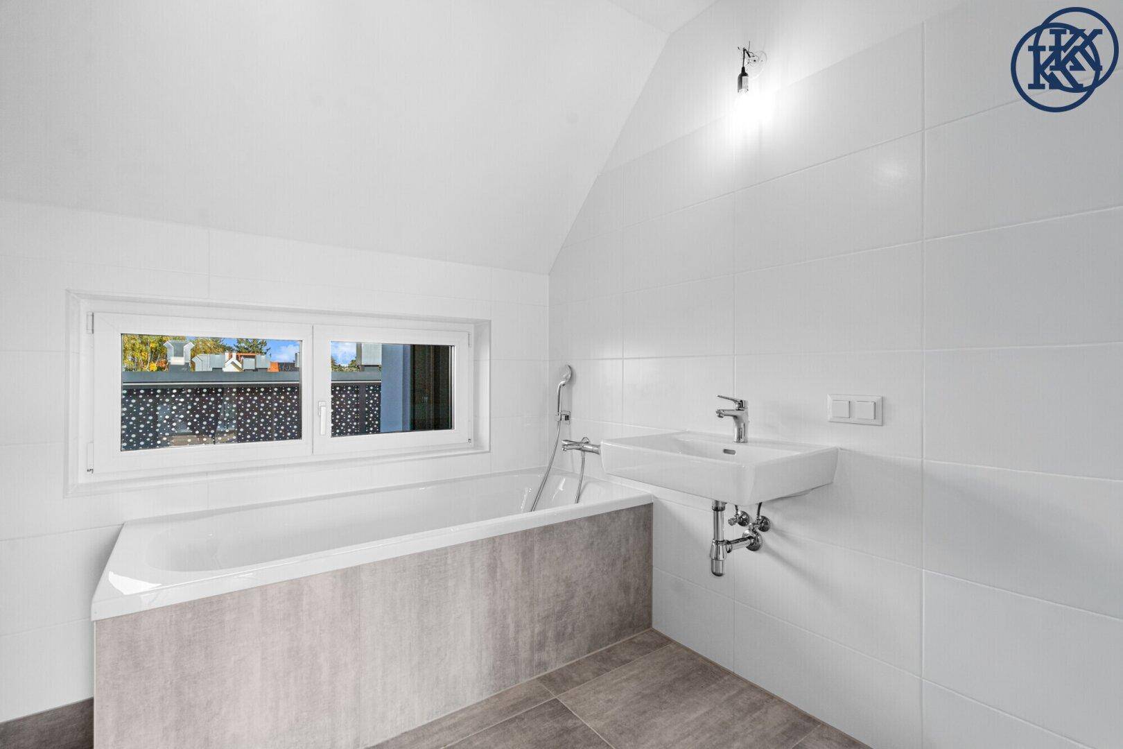 Helles Badezimmer mit Badewanne, Waschbecken und Fenster, ausgestattet mit modernen Fliesen.