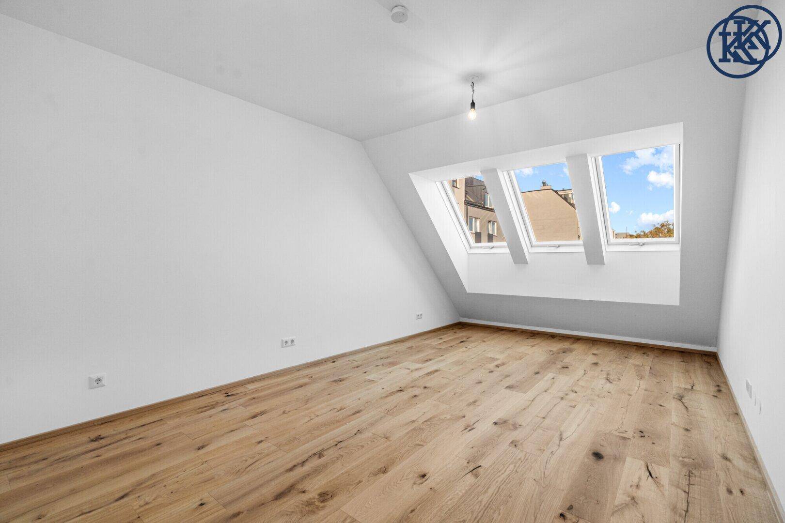 Leeres Schlafzimmer mit Holzboden, Dachschrägen und drei Dachfenstern, sehr hell und geräumig.