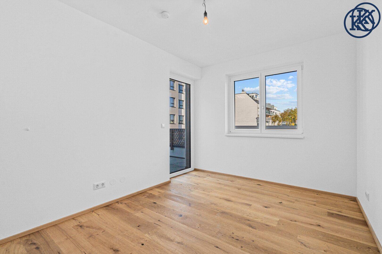 Leeres Zimmer mit Holzboden und Zugang zu einem Außenbereich, hell und modern gestaltet.