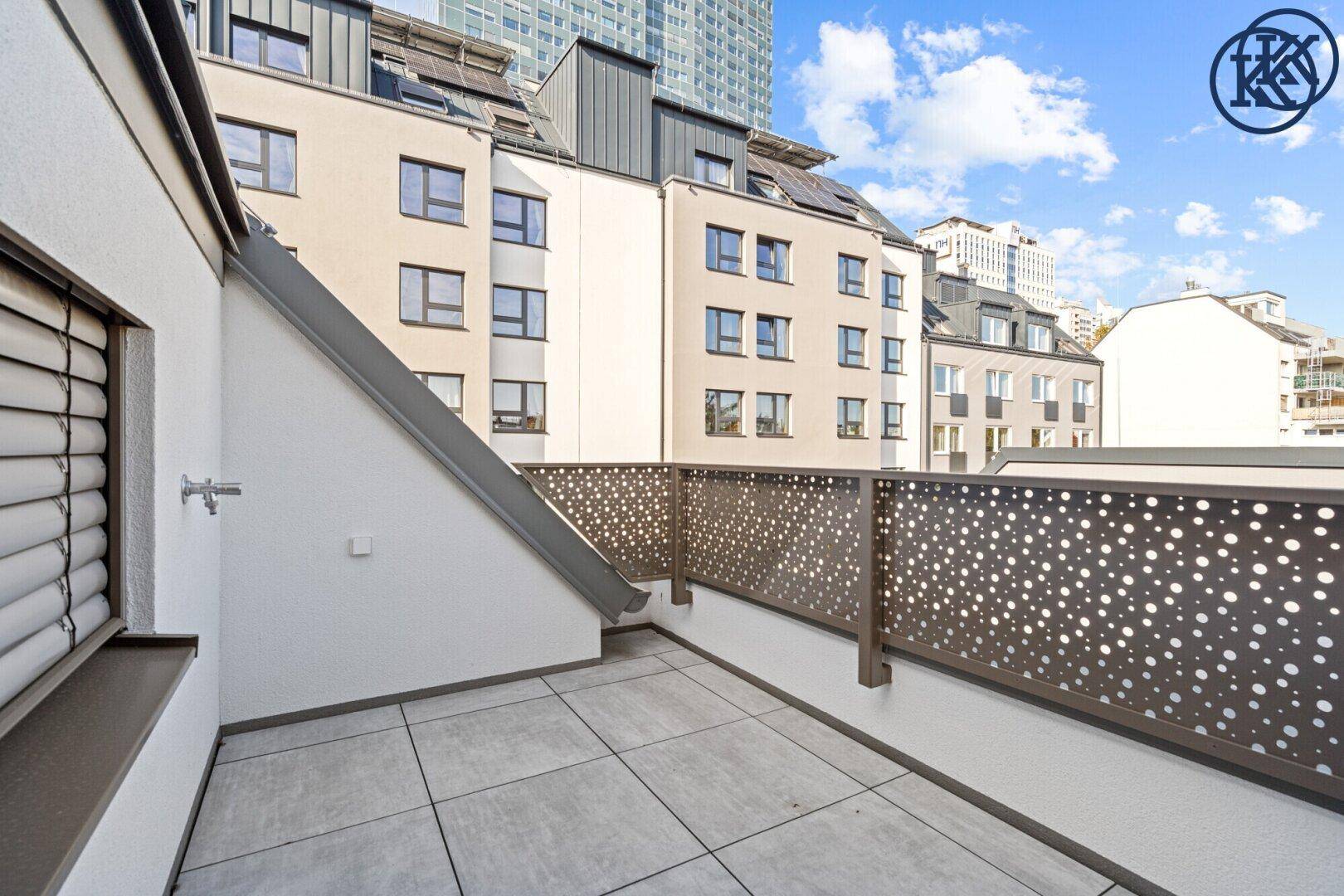 Geräumige Terrasse mit modernen Fliesen und dekorativem Geländer, umgeben von Gebäuden.