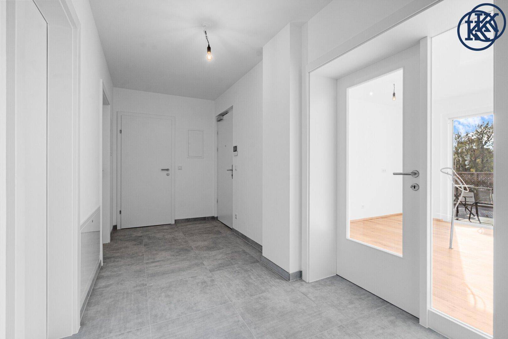 Heller Flur mit grauen Fliesen, weißen Wänden und Zugang zu einem Raum mit Balkon.