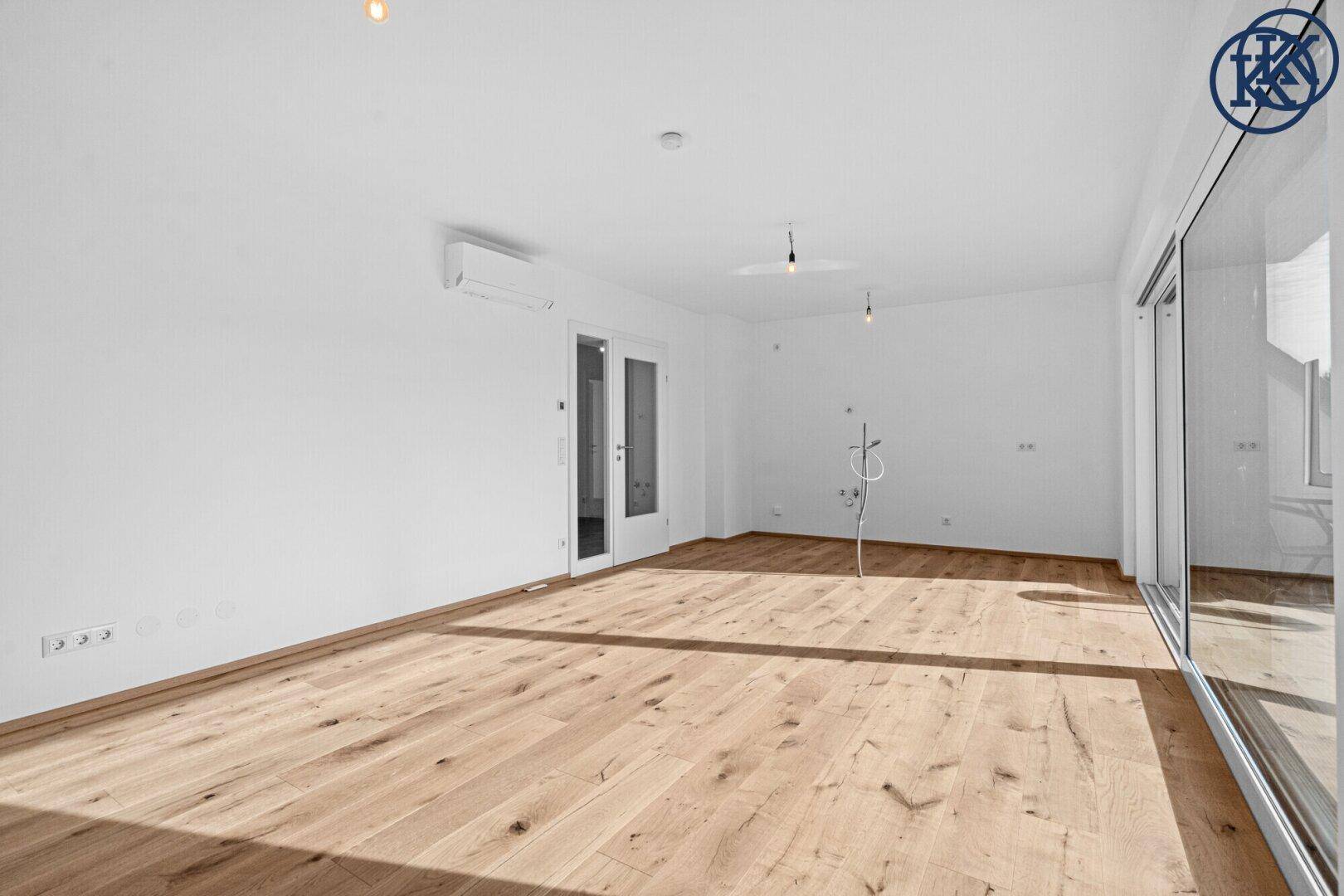 Helles, leeres Zimmer mit Holzboden und großen Fenstern, bereit zur individuellen Gestaltung.