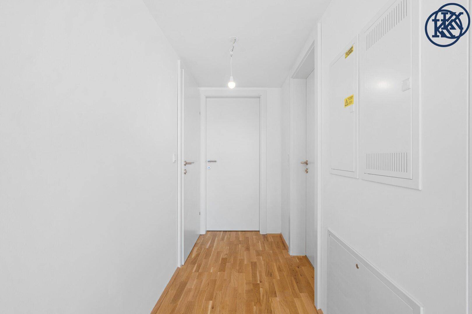Heller Flur mit Holzboden und weißen Wänden, der zu weiteren Räumen führt.