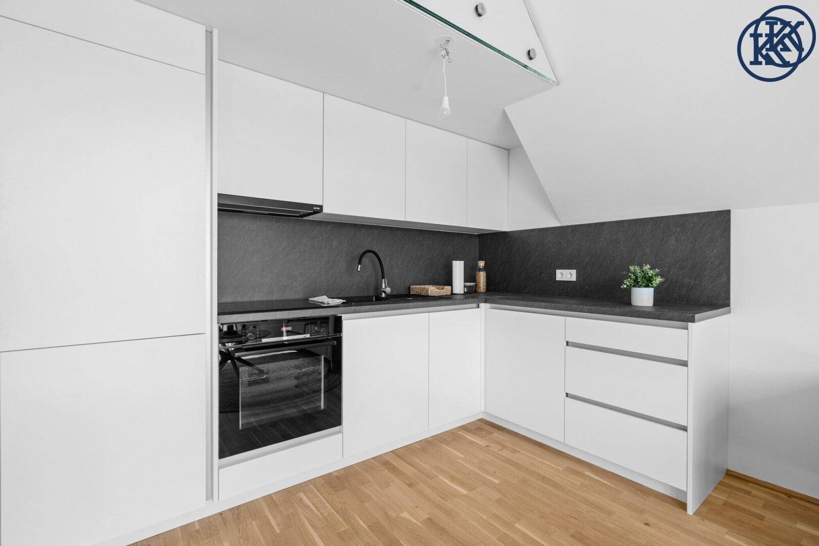 Moderne Einbauküche mit weißen Schränken, dunkler Arbeitsplatte und integriertem Backofen.