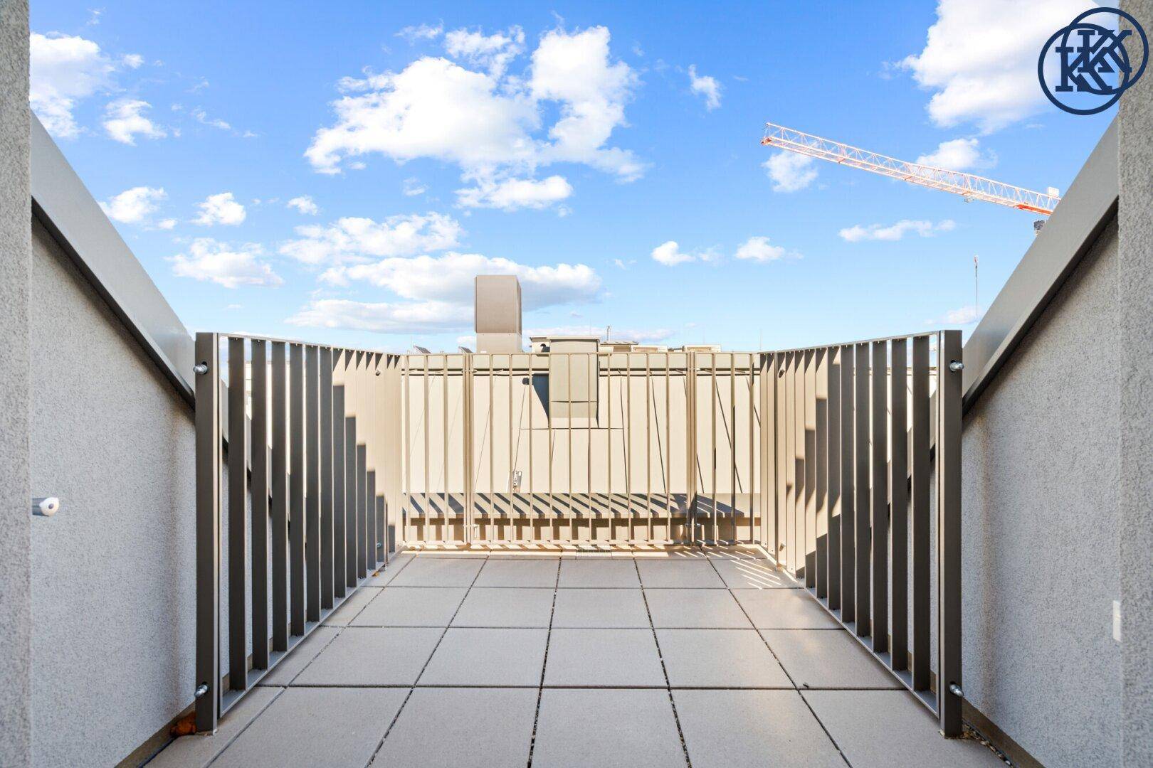 Sonnige Dachterrasse mit Fliesenboden und Blick auf die Umgebung und einen Kran.