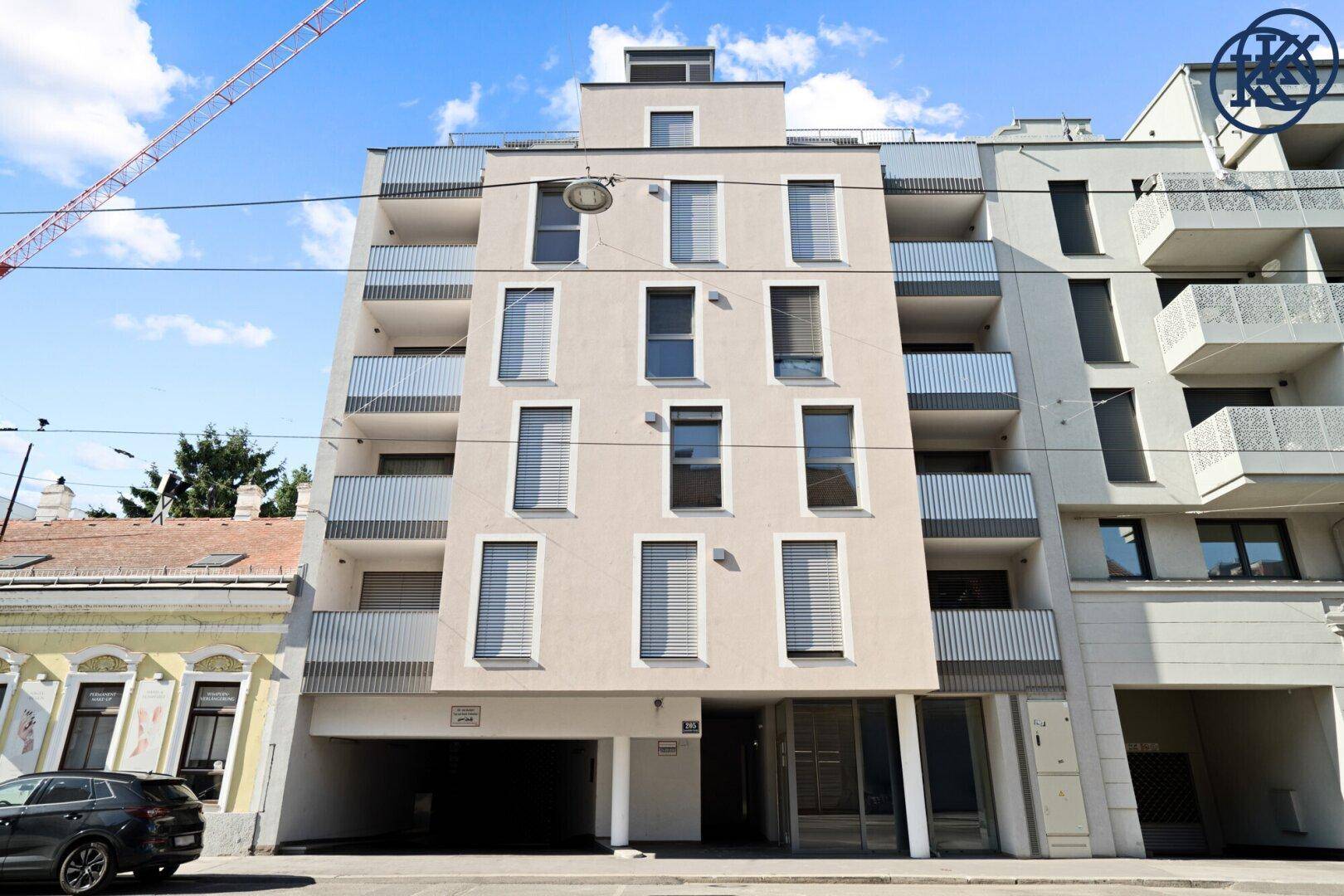 Moderne Wohnhausfassade mit Balkonen und großen Fenstern in städtischer Umgebung.