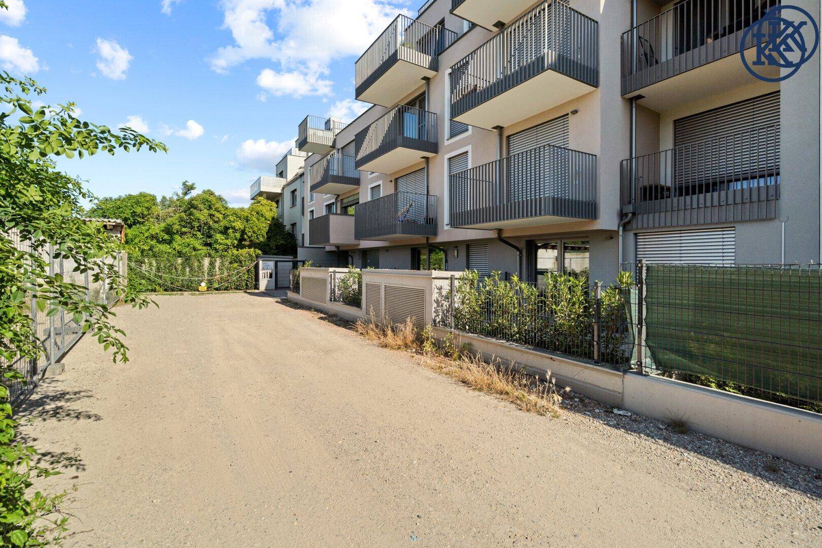 Seitenansicht eines modernen Wohngebäudes mit Parkplatz und viel Grün.