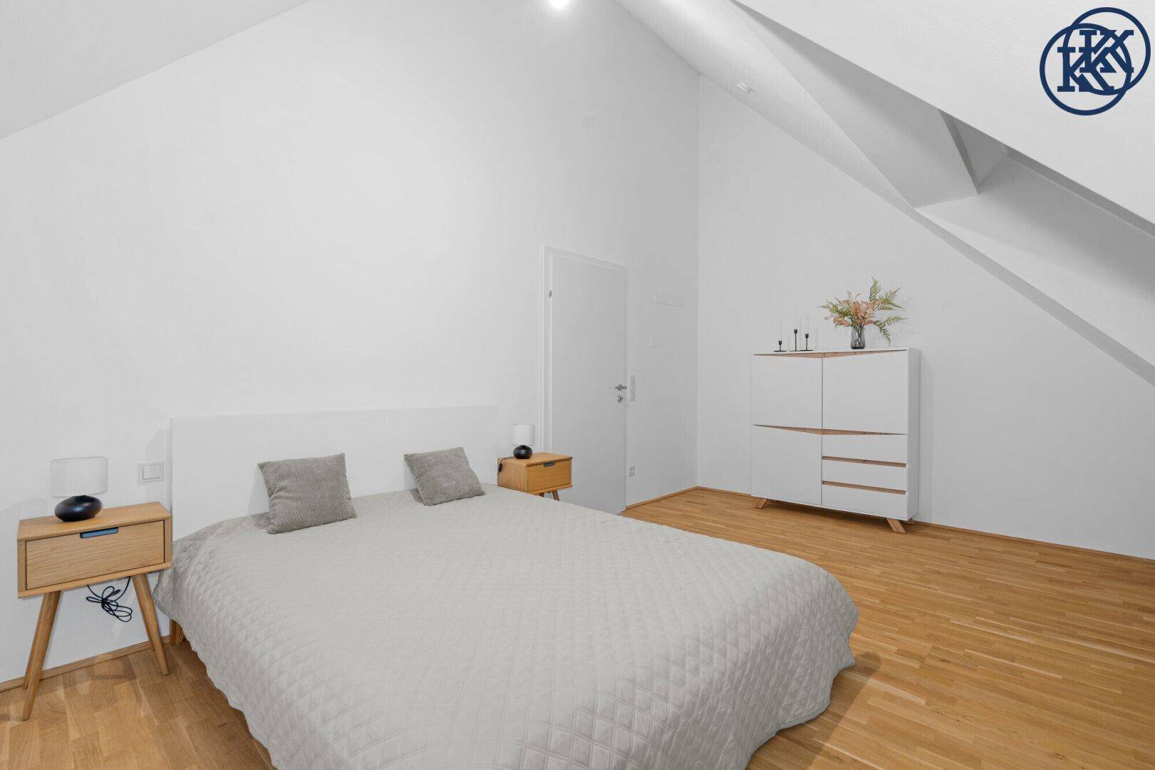 Helles Schlafzimmer mit Holzboden, weißem Bett und schrägen Wänden im Dachgeschoss.