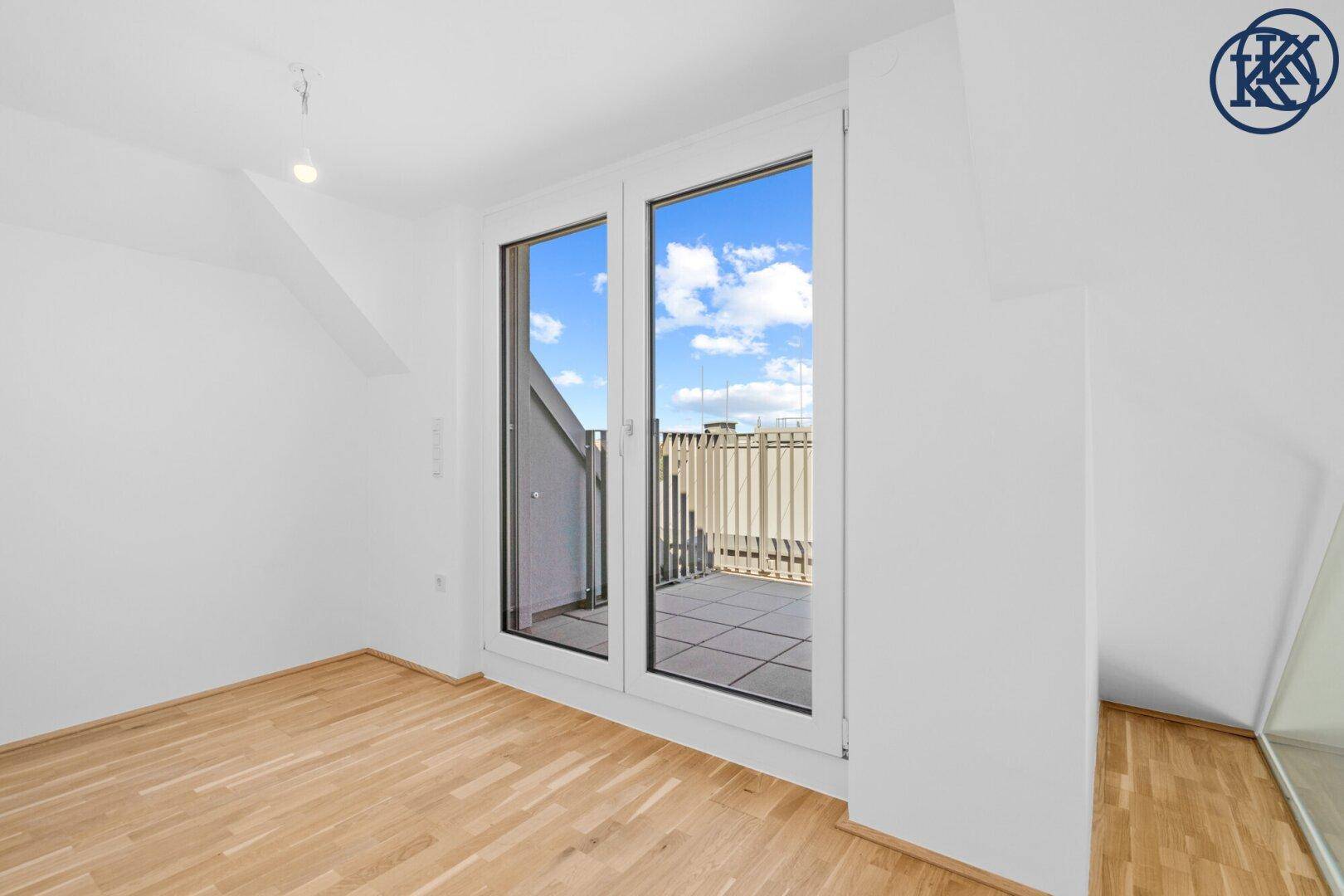 Heller Raum mit Holzboden und Zugang zu einer Terrasse durch große Fenstertüren.