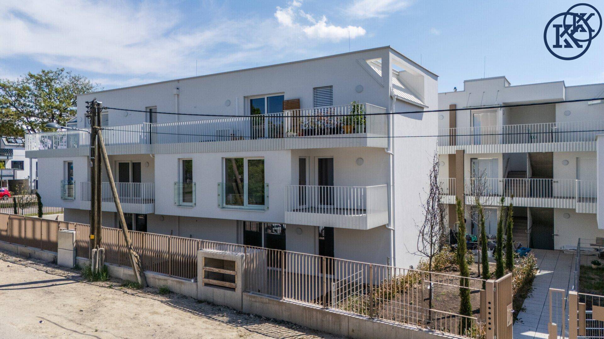 Moderne Wohnanlage mit weißer Fassade, Balkonen und großen Fenstern von oben betrachtet.