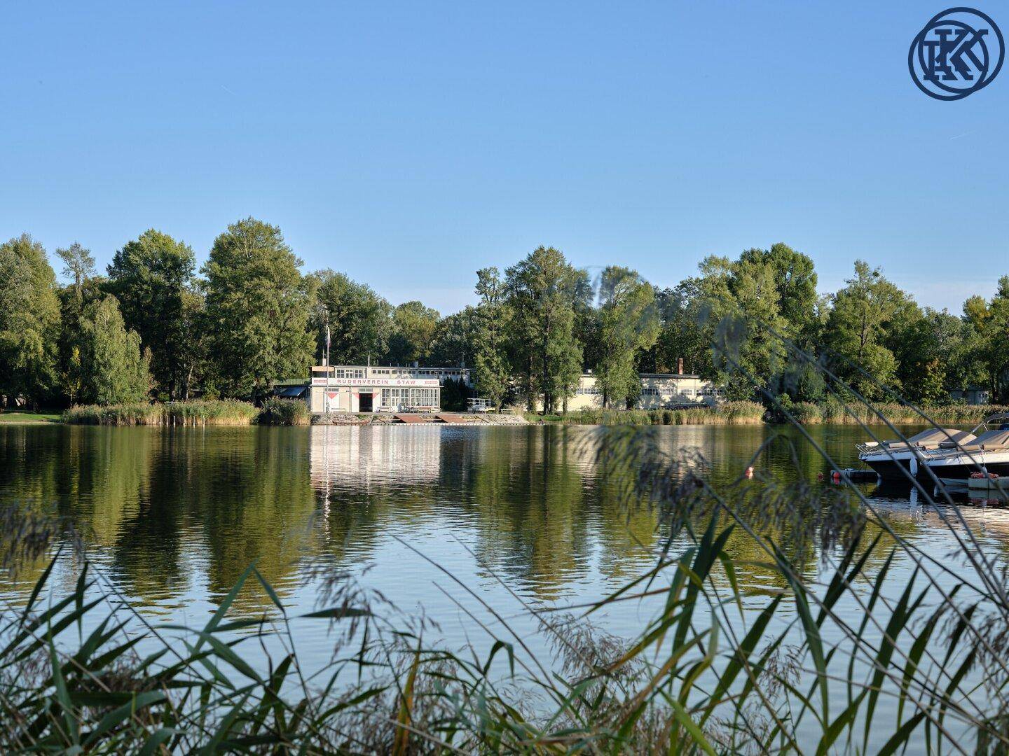 Idyllischer See mit einem Gebäude am gegenüberliegenden Ufer, umgeben von üppiger Natur.