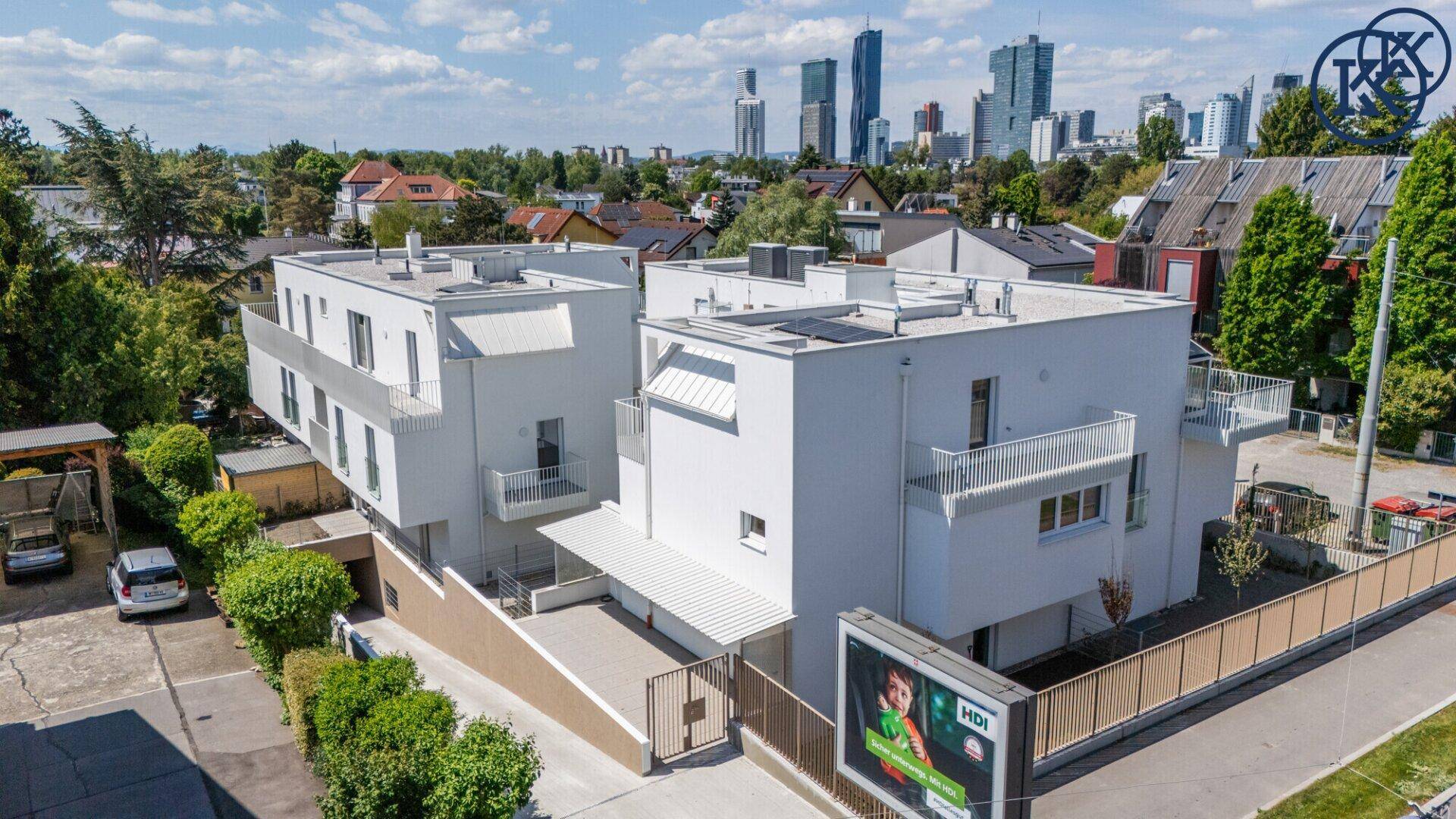 Moderne Wohnanlage mit Tiefgaragenzufahrt und Stadtblick im Hintergrund unter blauem Himmel.