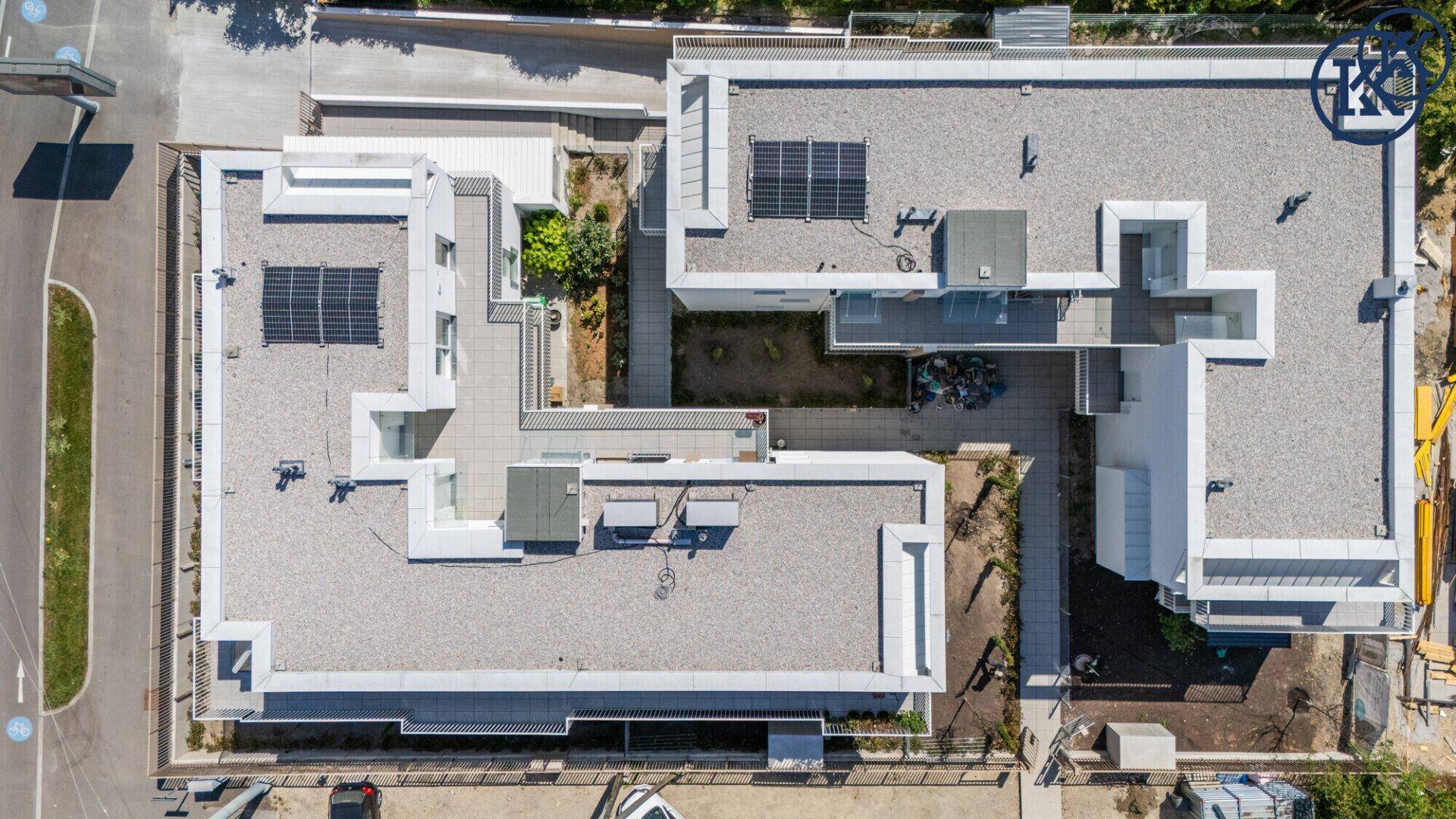 Draufsicht auf die Flachdächer der modernen Wohnanlage mit Solarpaneelen und Innenhof.