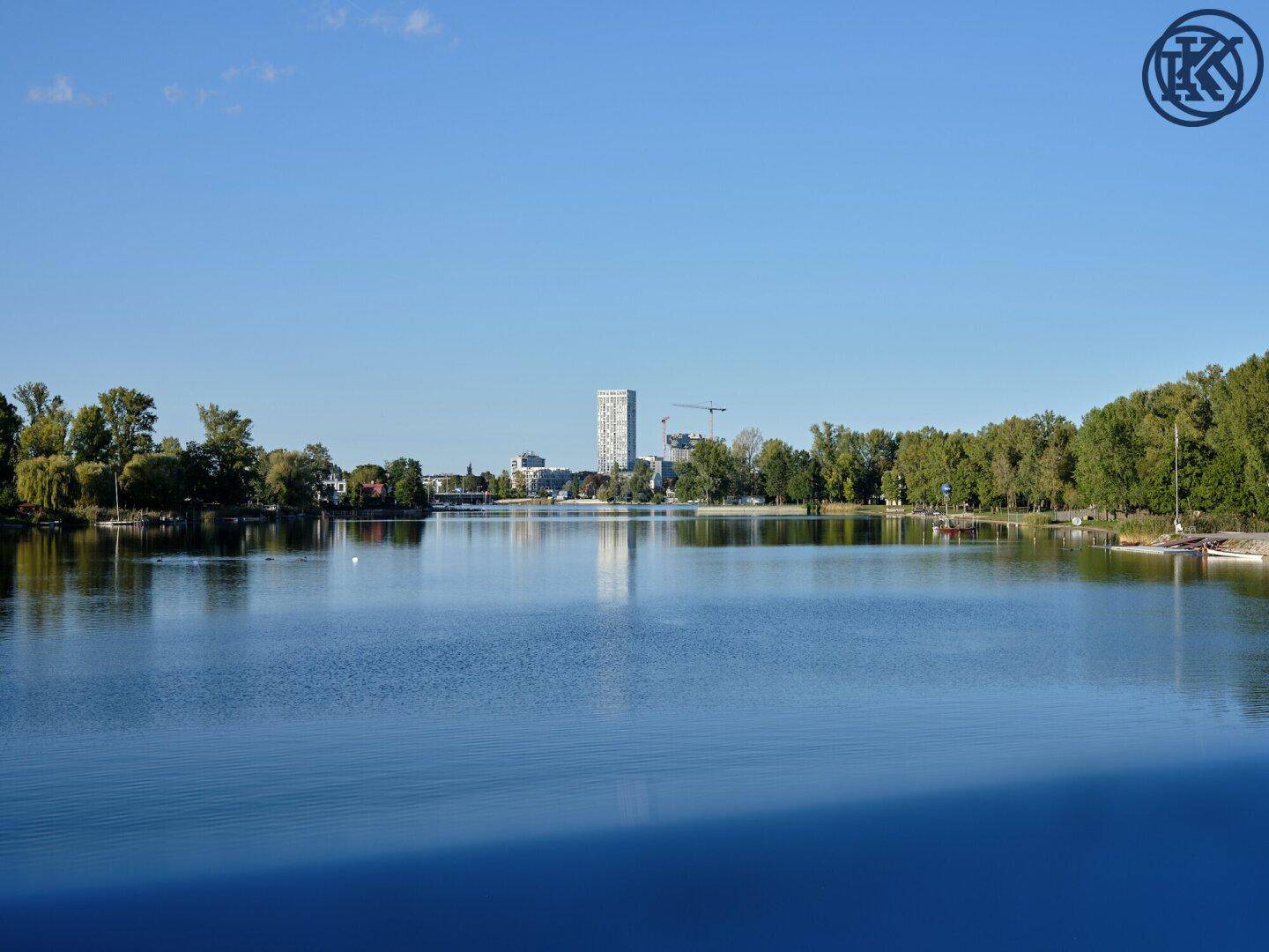 Ruhiger See mit der Silhouette von Stadtgebäuden am Horizont unter blauem Himmel.